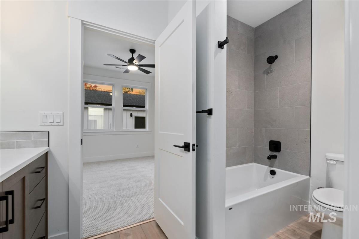 Bathroom featuring light wood-style flooring, vanity, washtub / shower combination, and a ceiling fan