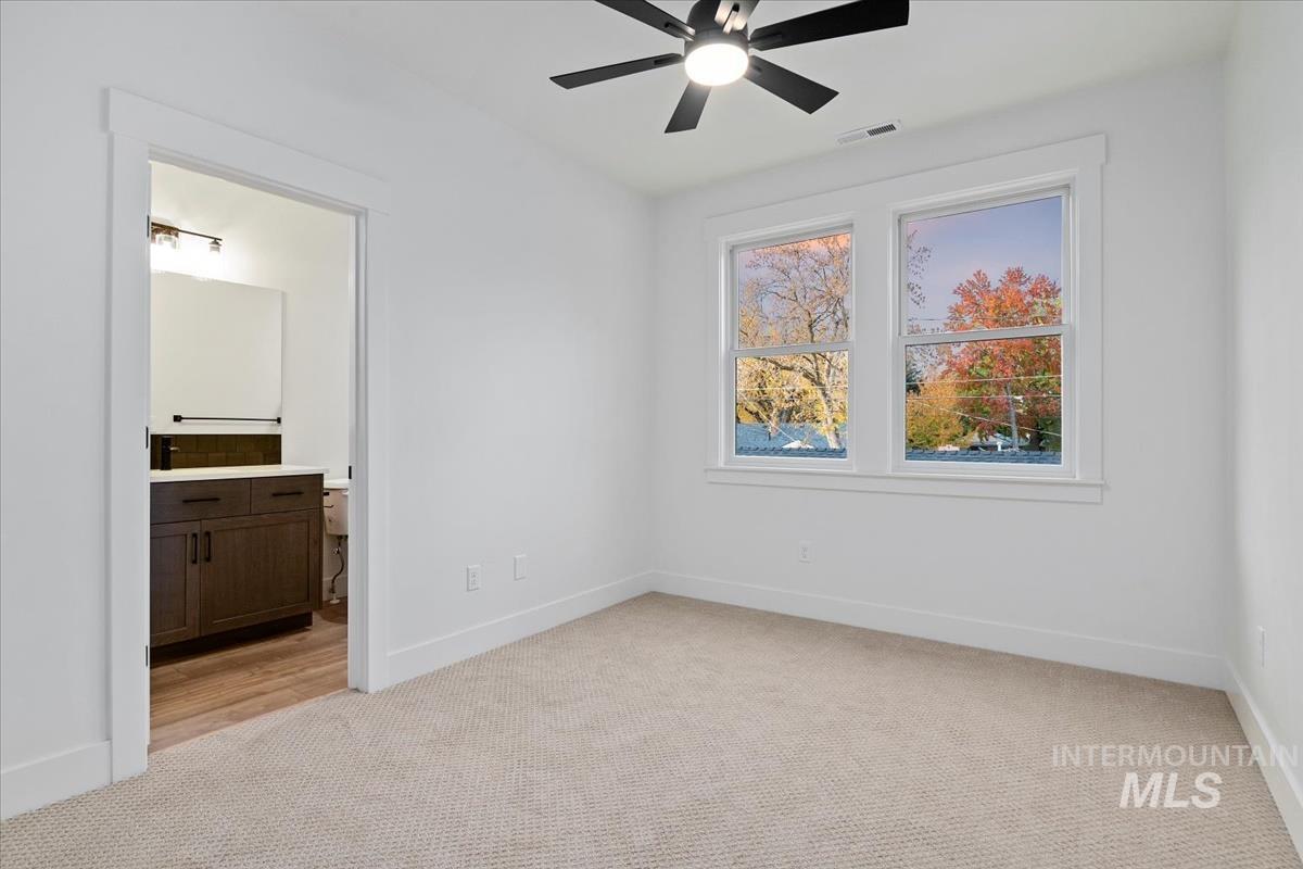 Unfurnished bedroom with light colored carpet, ensuite bath, and a ceiling fan