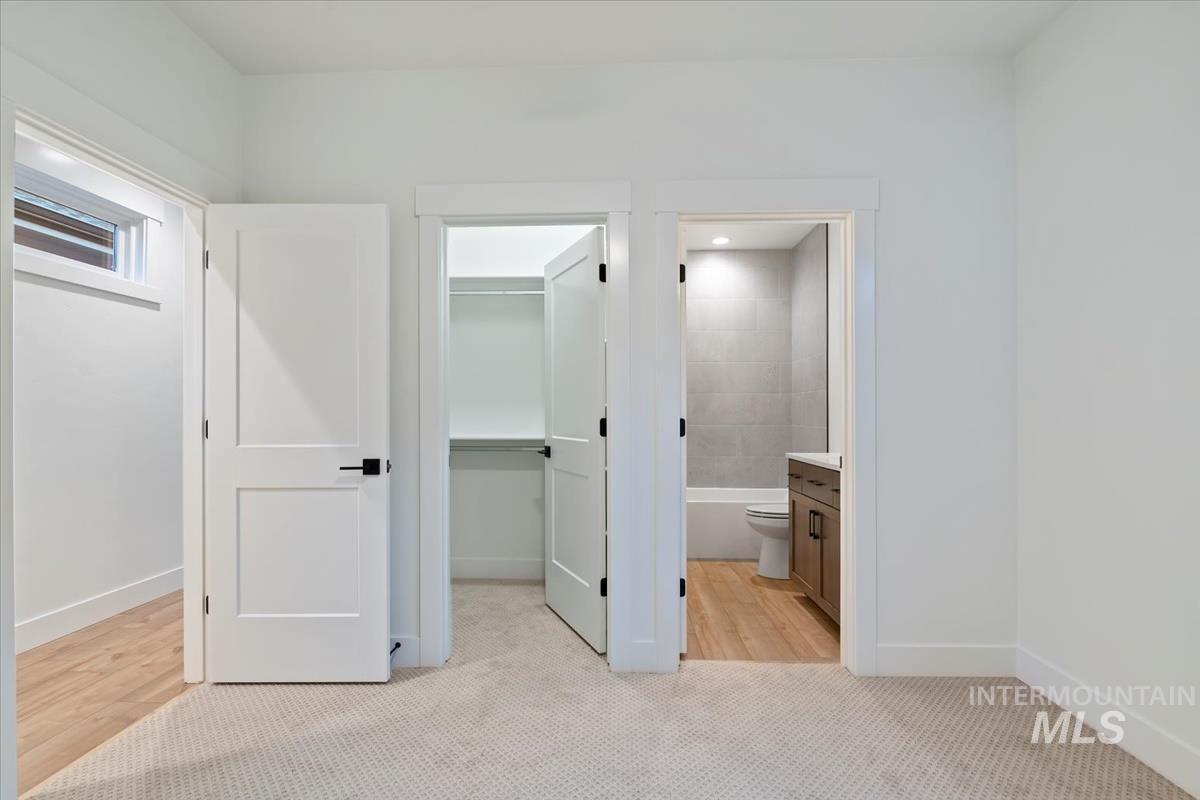Unfurnished bedroom featuring a walk in closet, light carpet, and ensuite bath
