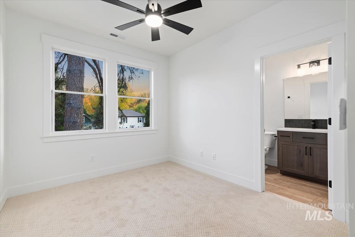 Unfurnished bedroom with light carpet, ensuite bathroom, and ceiling fan