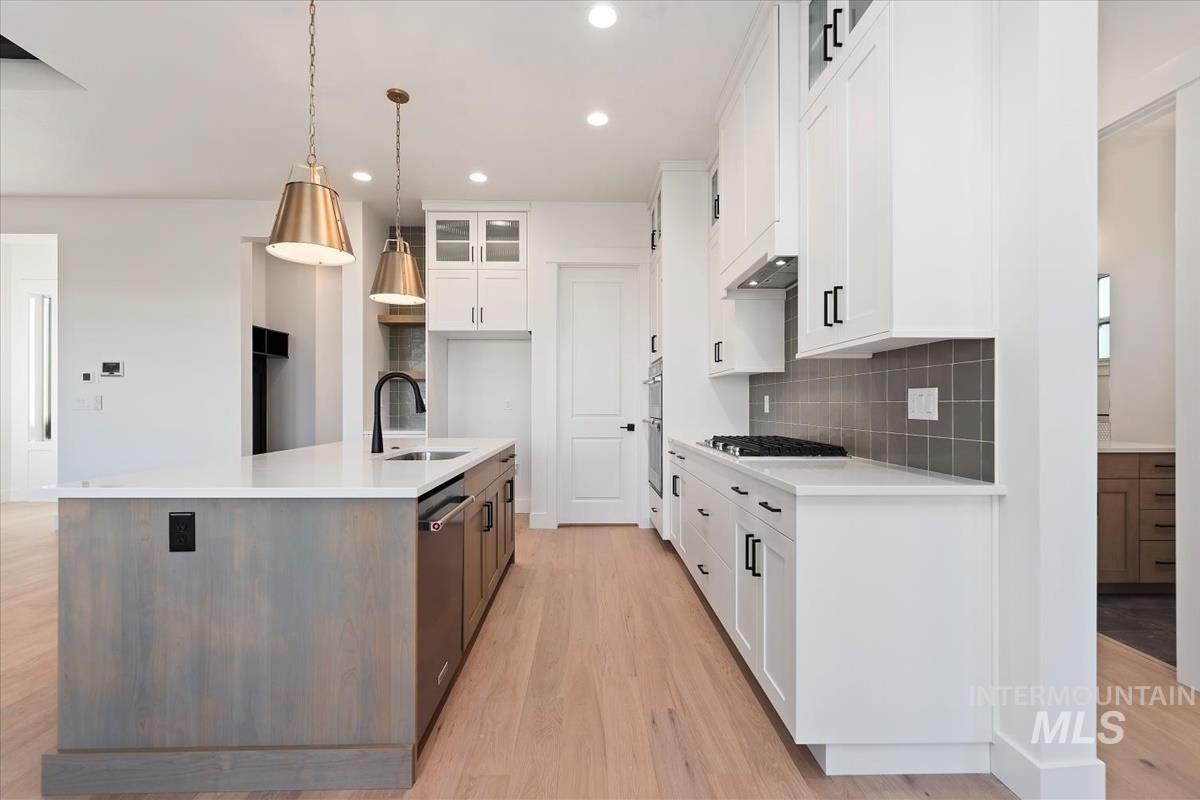Kitchen with glass insert cabinets, white cabinets, a center island with sink, light wood finished floors, and recessed lighting