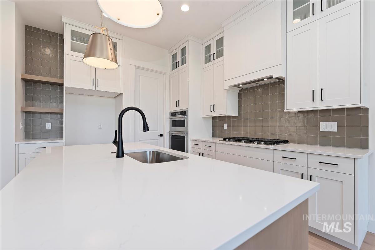 Kitchen featuring glass insert cabinets, white cabinets, and decorative backsplash