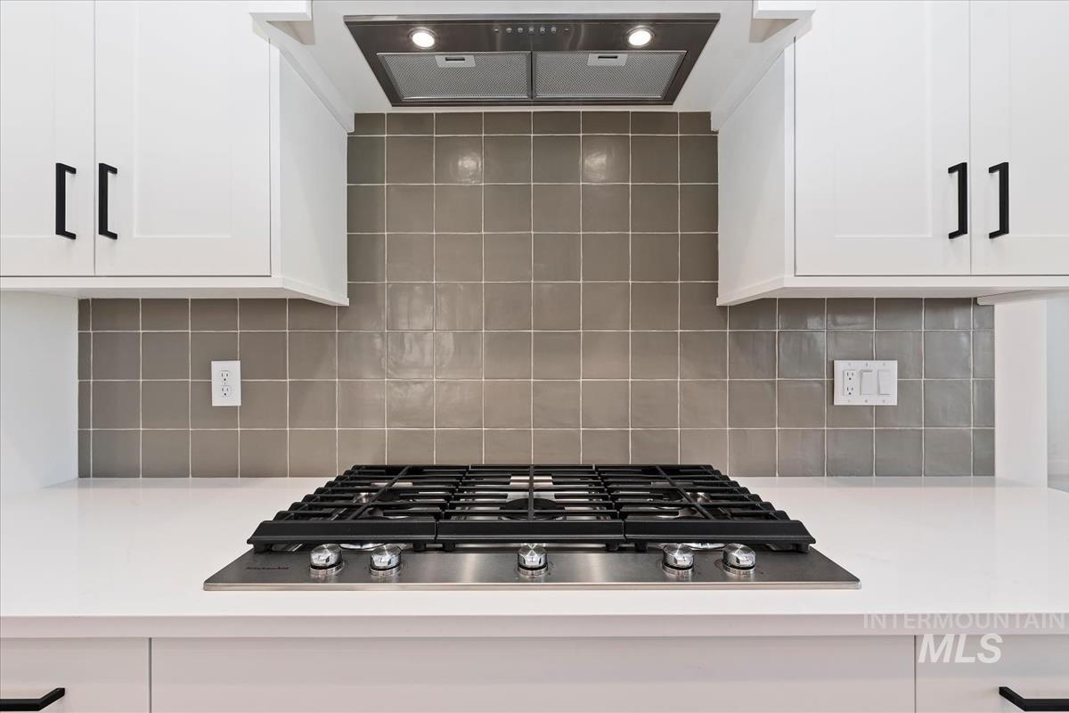 Kitchen with ventilation hood, stainless steel gas cooktop, white cabinetry, and tasteful backsplash