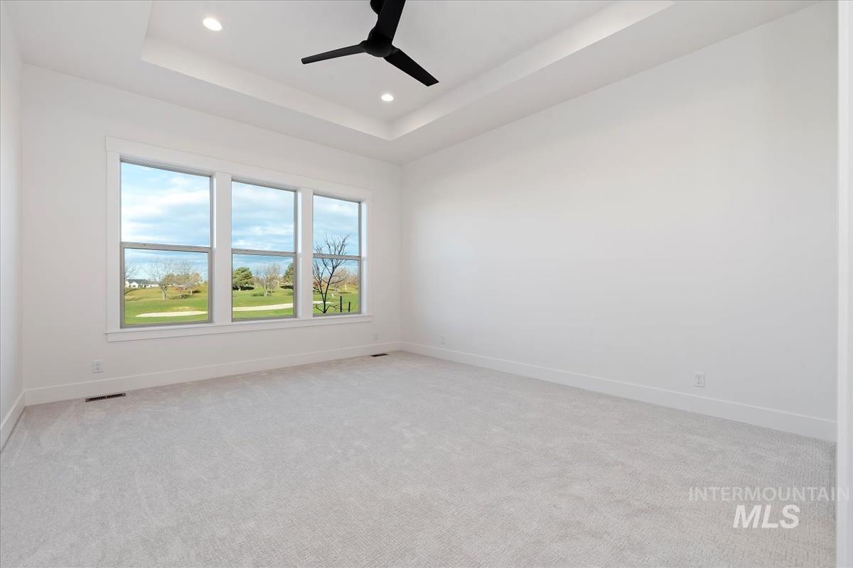 Empty room with a raised ceiling, light colored carpet, recessed lighting, ceiling fan, and a water view