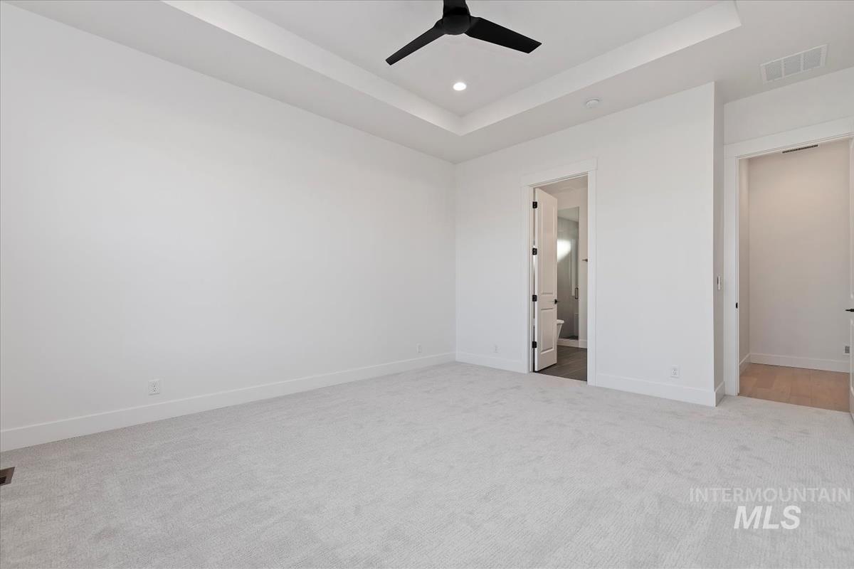 Unfurnished bedroom featuring a tray ceiling, light carpet, ceiling fan, recessed lighting, and connected bathroom
