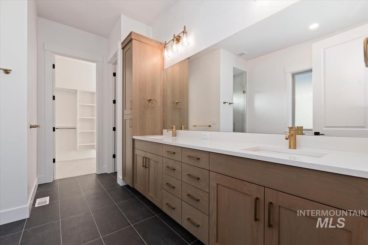 Full bathroom with double vanity, dark tile patterned flooring, a stall shower, and a spacious closet