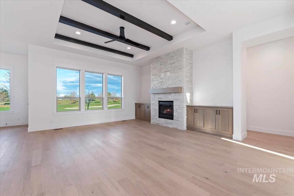 Unfurnished living room with a raised ceiling, light wood-style floors, a fireplace, and recessed lighting