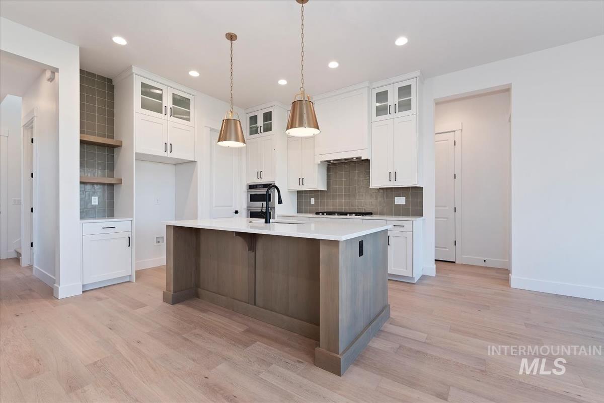 Kitchen with backsplash, white cabinets, a kitchen bar, an island with sink, and recessed lighting