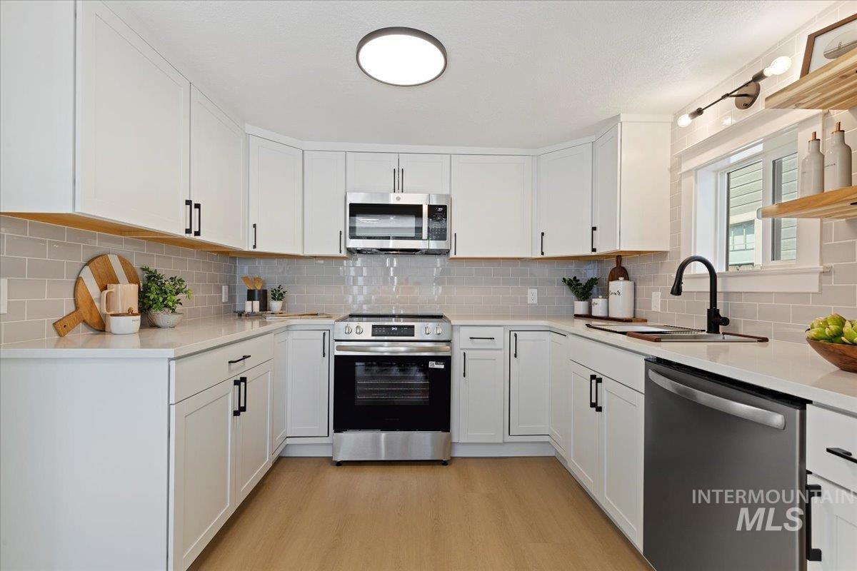 Kitchen with stainless steel appliances, white cabinets, light wood-style flooring, and light stone countertops