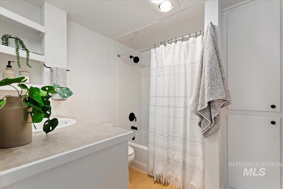 Full bath with tile walls, shower / bath combo, vanity, and light wood-style floors