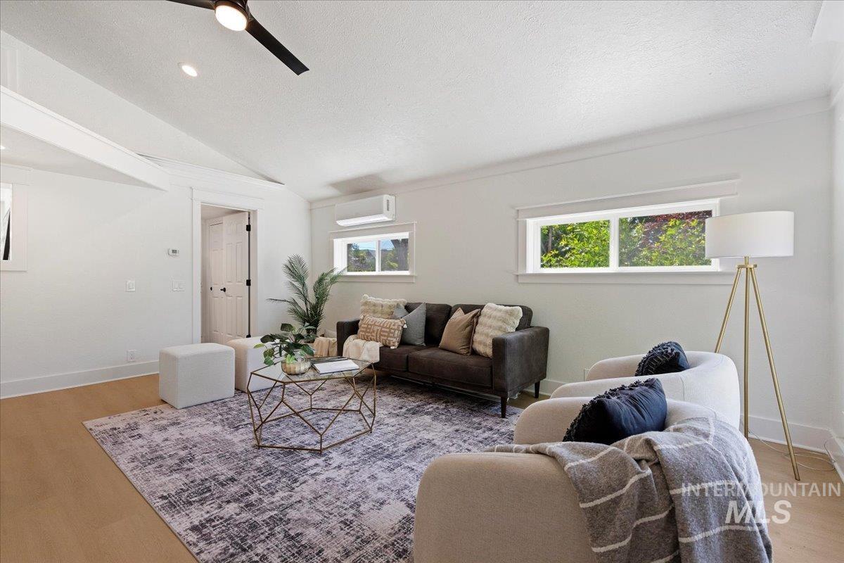 Living room with light wood finished floors, lofted ceiling, a textured ceiling, ceiling fan, and an AC wall unit