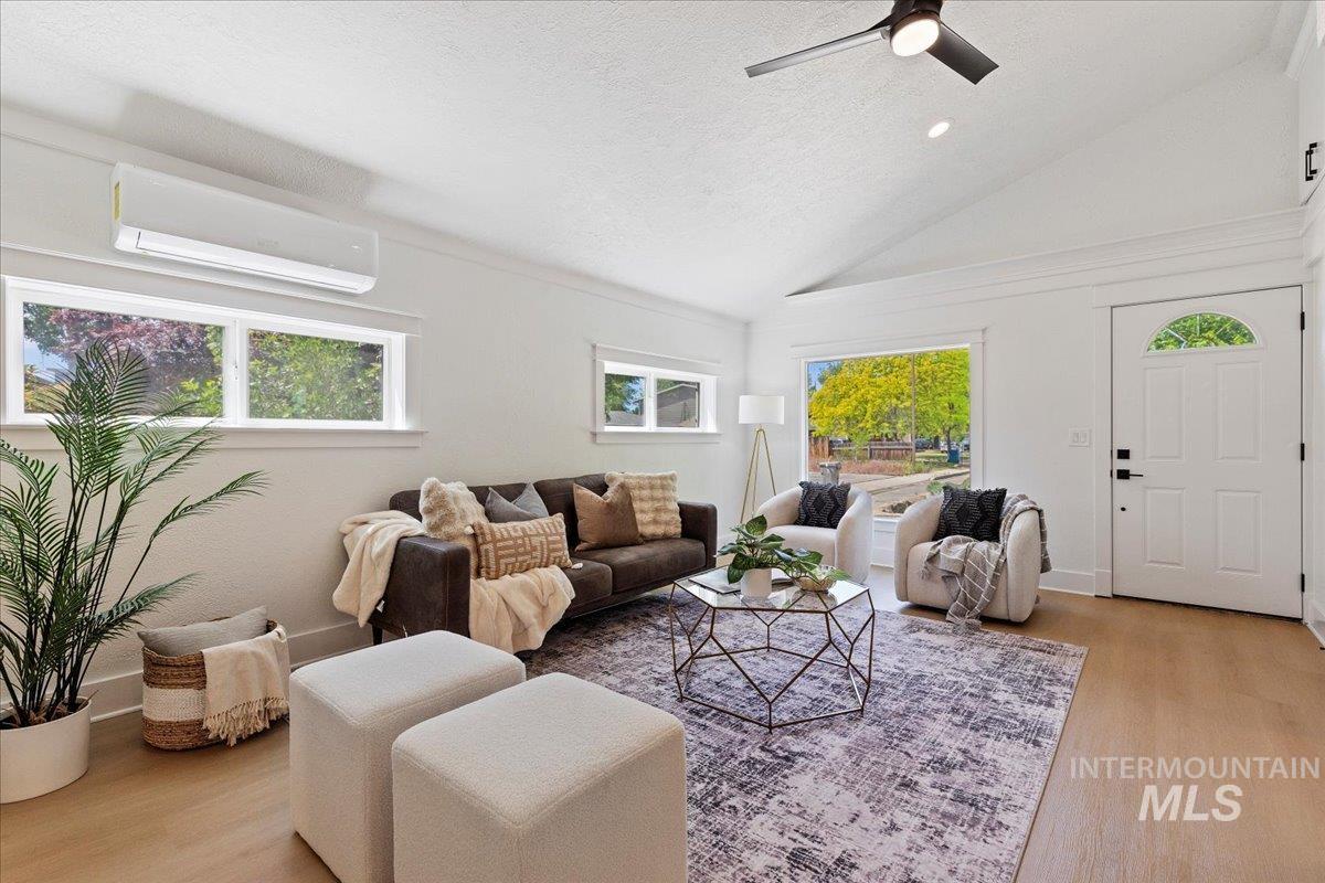 Living area featuring light wood-style flooring, plenty of natural light, an AC wall unit, high vaulted ceiling, and a textured ceiling