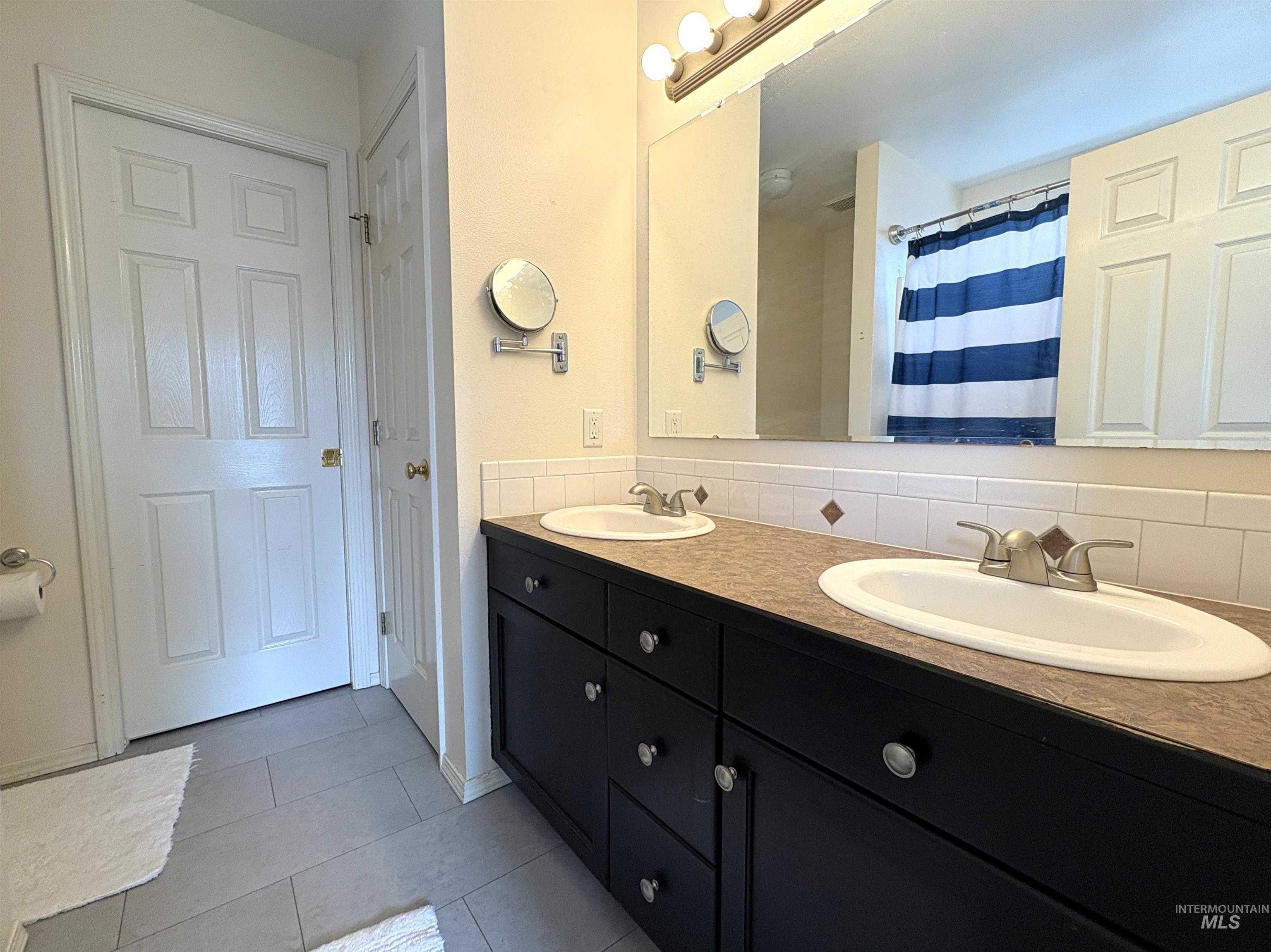 Full bath with a shower with curtain, double vanity, decorative backsplash, and light tile patterned floors