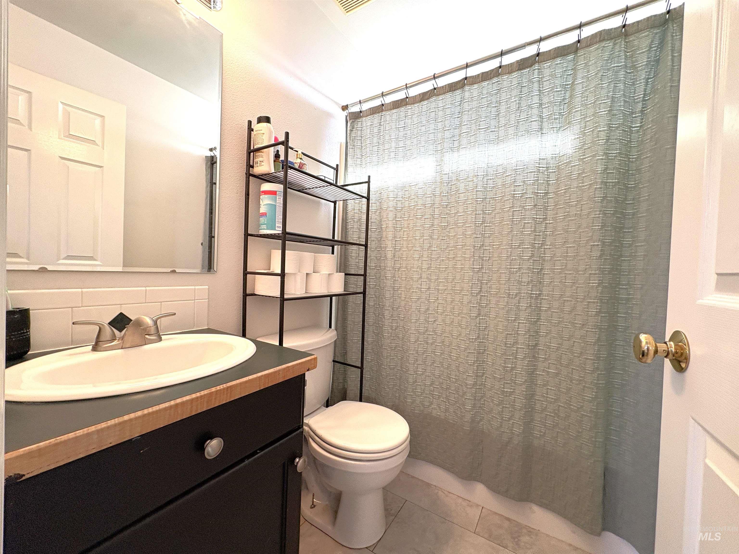 Full bath with a shower with curtain, vanity, tile patterned flooring, and decorative backsplash
