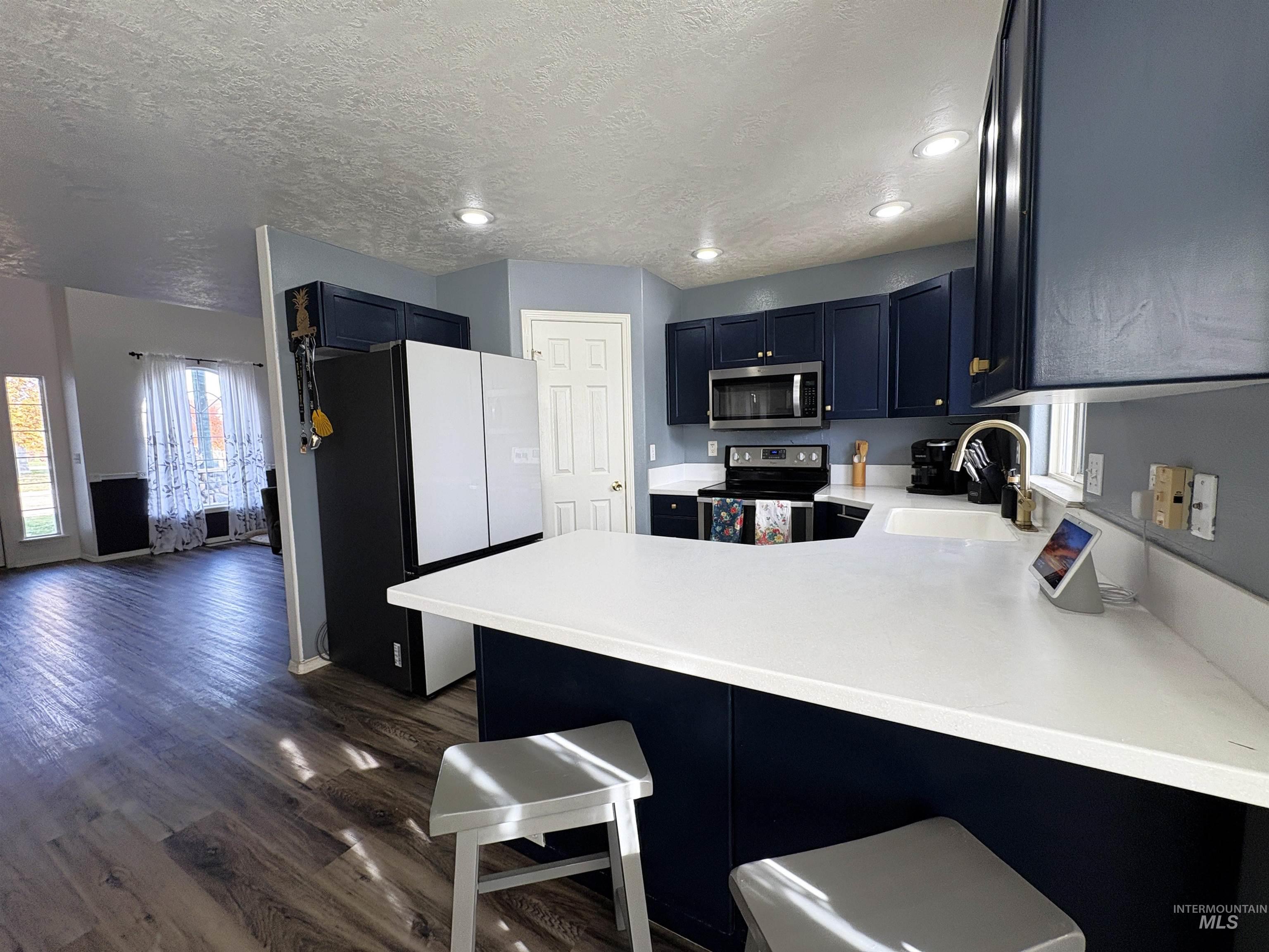 Kitchen with stainless steel appliances, a breakfast bar area, a peninsula, dark wood finished floors, and plenty of natural light
