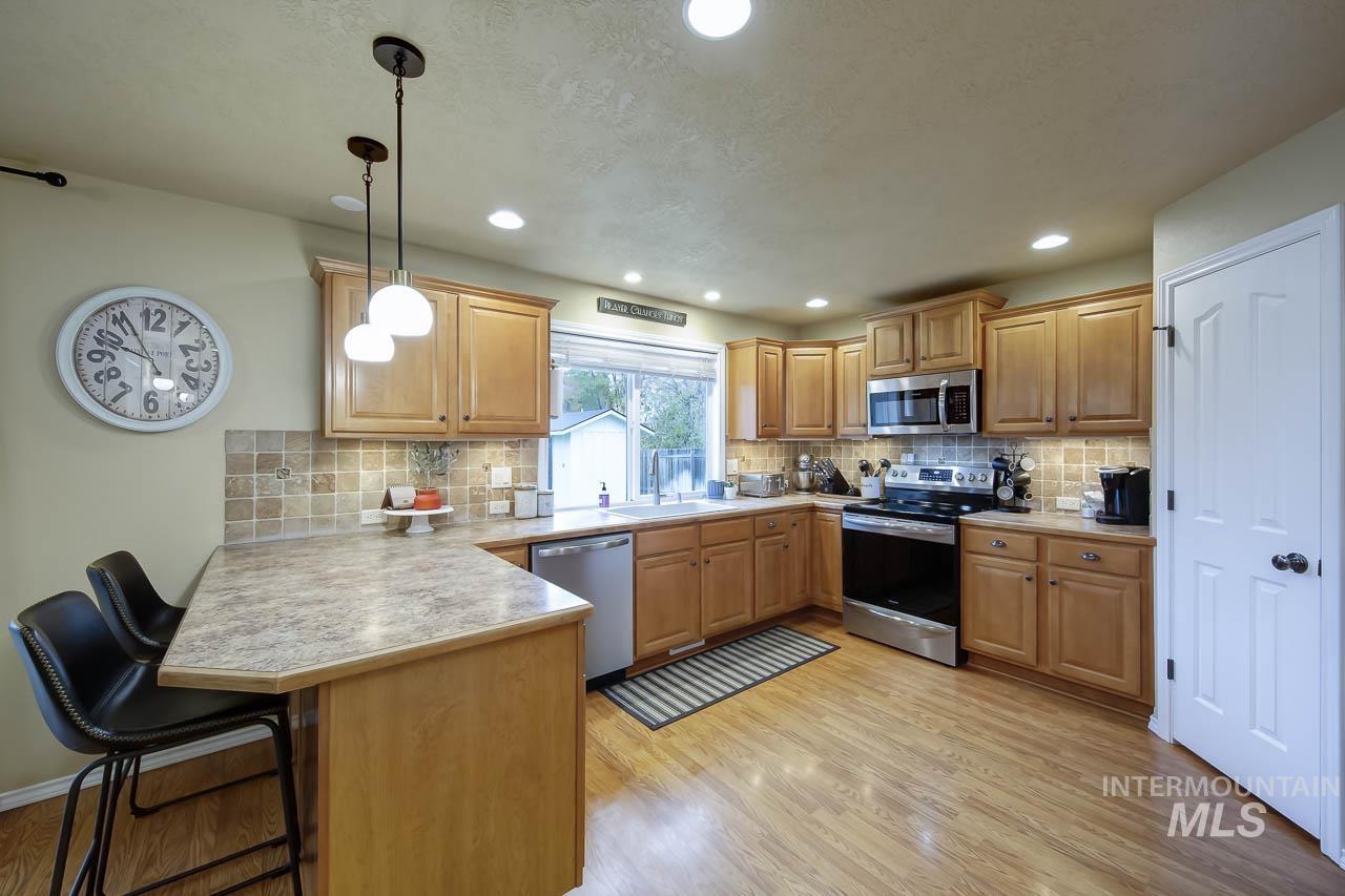Kitchen with a kitchen breakfast bar, stainless steel appliances, hanging light fixtures, light countertops, and light wood-style floors