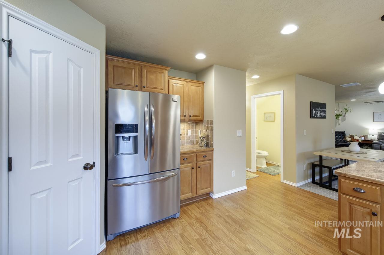 Kitchen featuring stainless steel fridge with ice dispenser, decorative backsplash, light wood-style flooring, light countertops, and recessed lighting