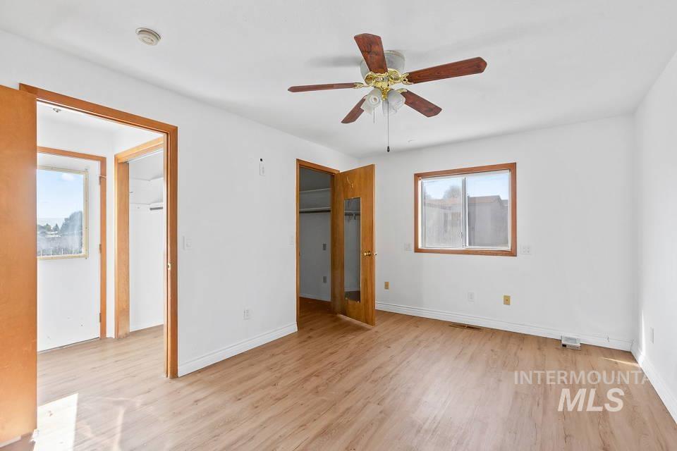Unfurnished bedroom with a walk in closet, light wood finished floors, and a ceiling fan