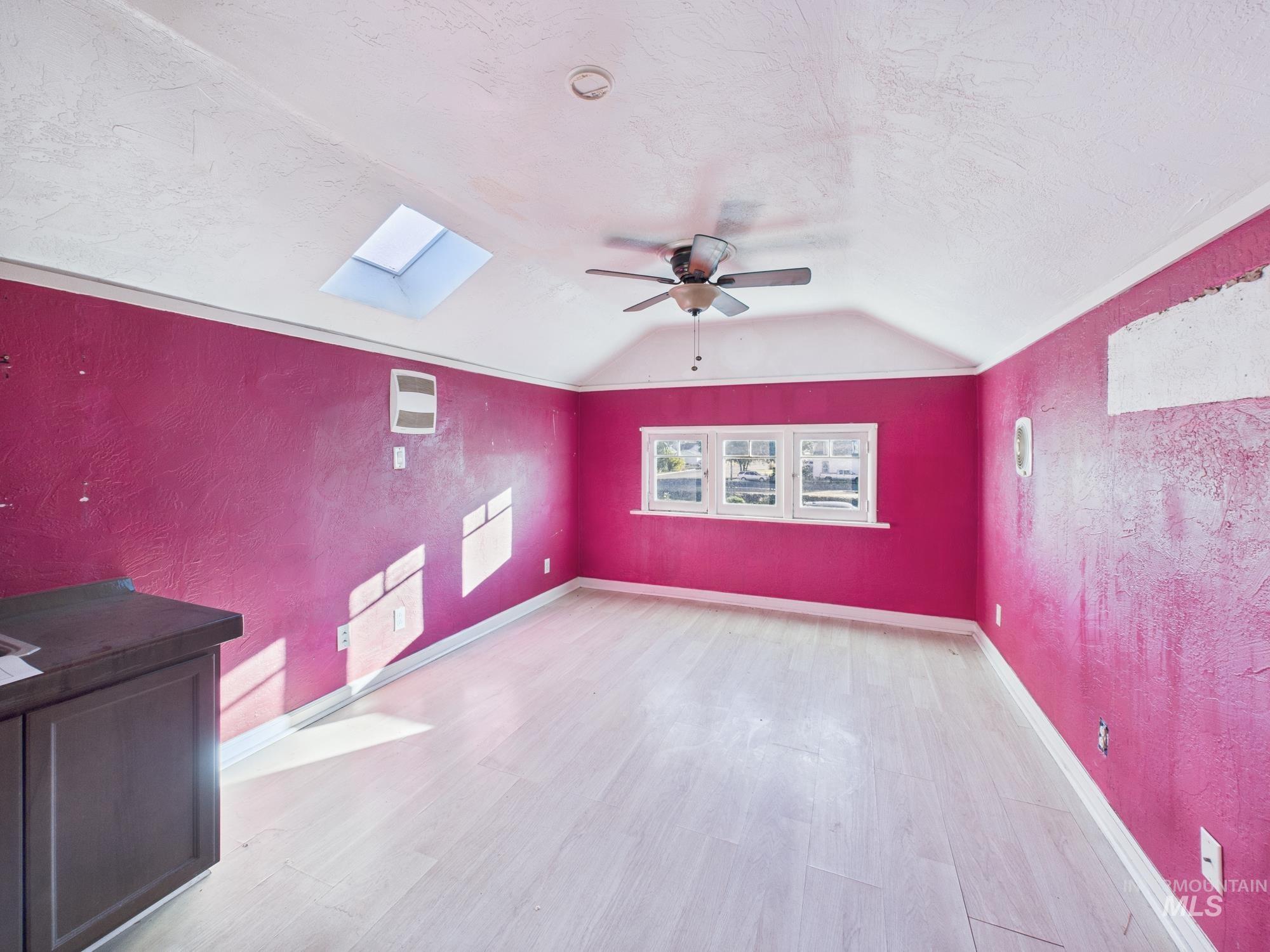 Unfurnished room featuring a textured wall, a skylight, light wood-style floors, a textured ceiling, and lofted ceiling