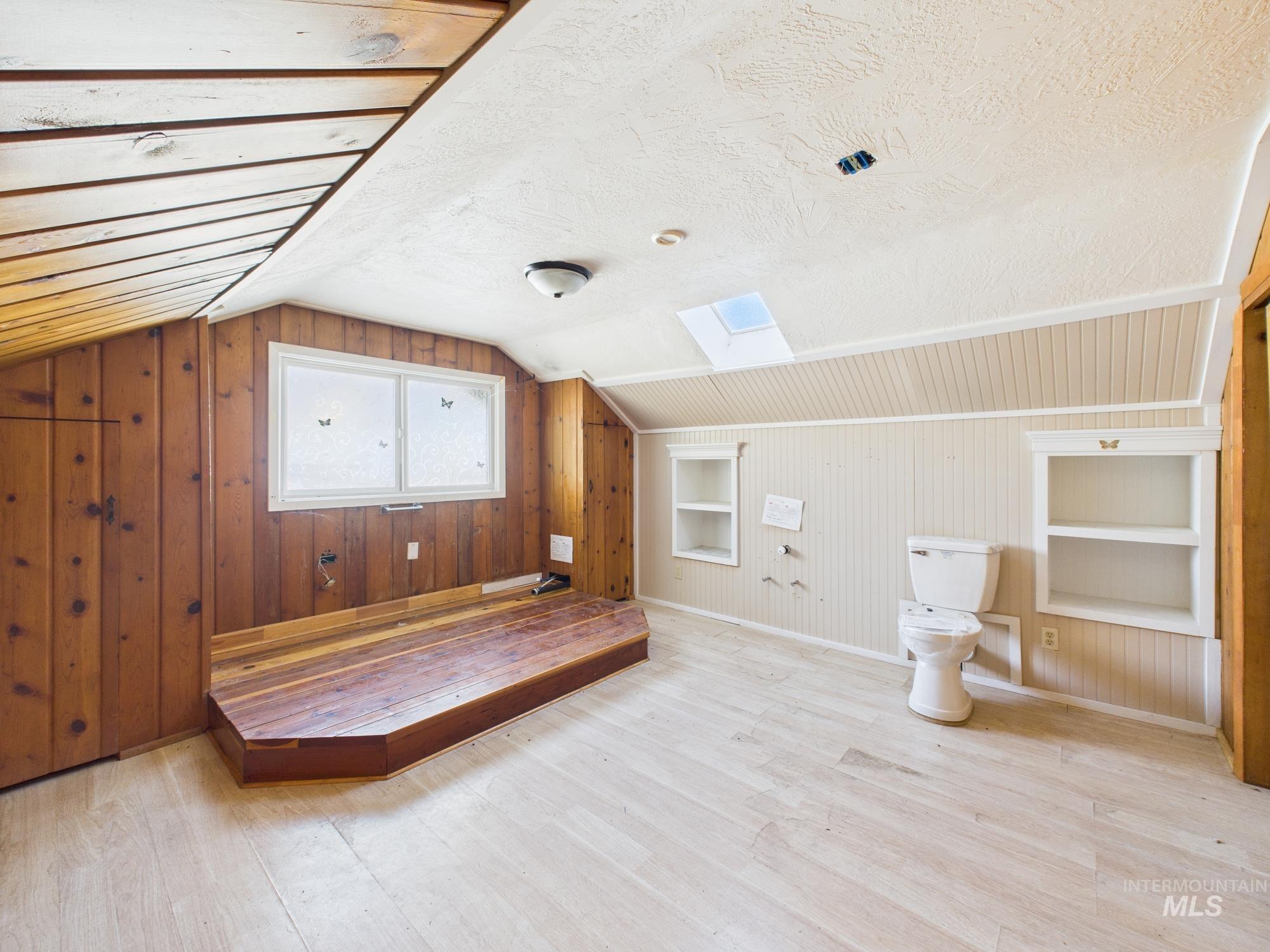 Additional living space with built in shelves, wood walls, a skylight, light wood-style floors, and lofted ceiling