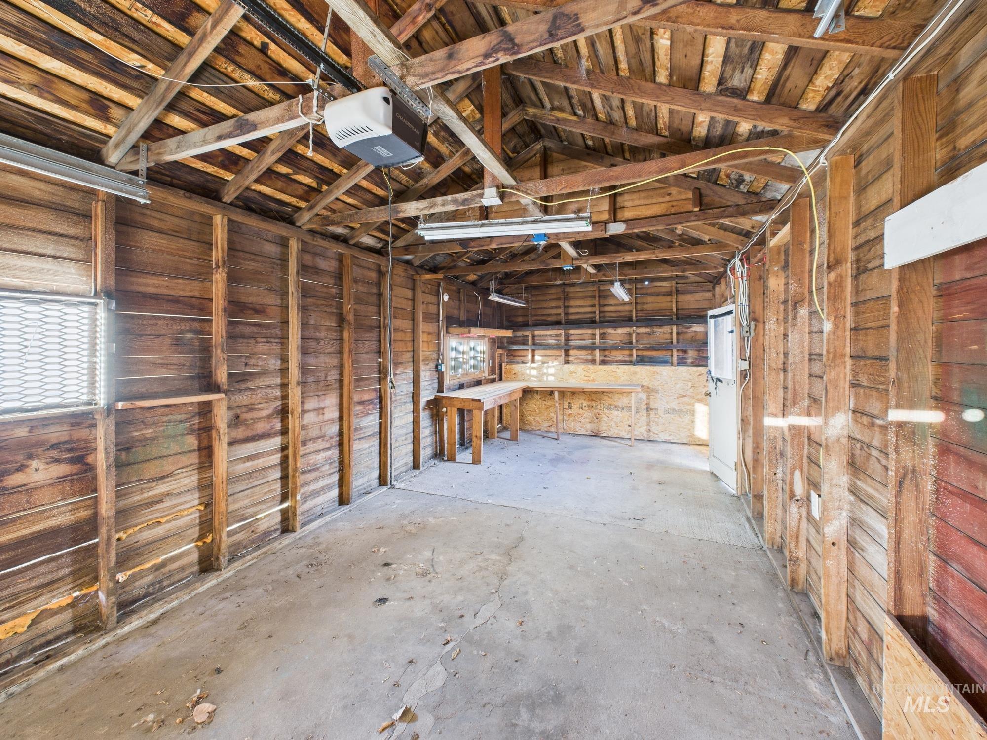 Misc room featuring a garage, unfinished concrete flooring, wooden walls, and lofted ceiling