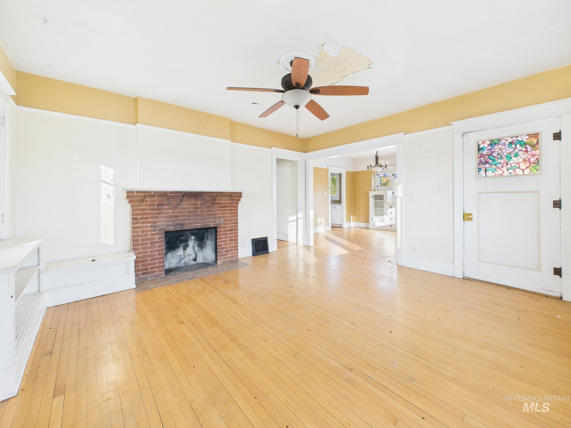 Unfurnished living room with light wood finished floors, a brick fireplace, a ceiling fan, and a chandelier