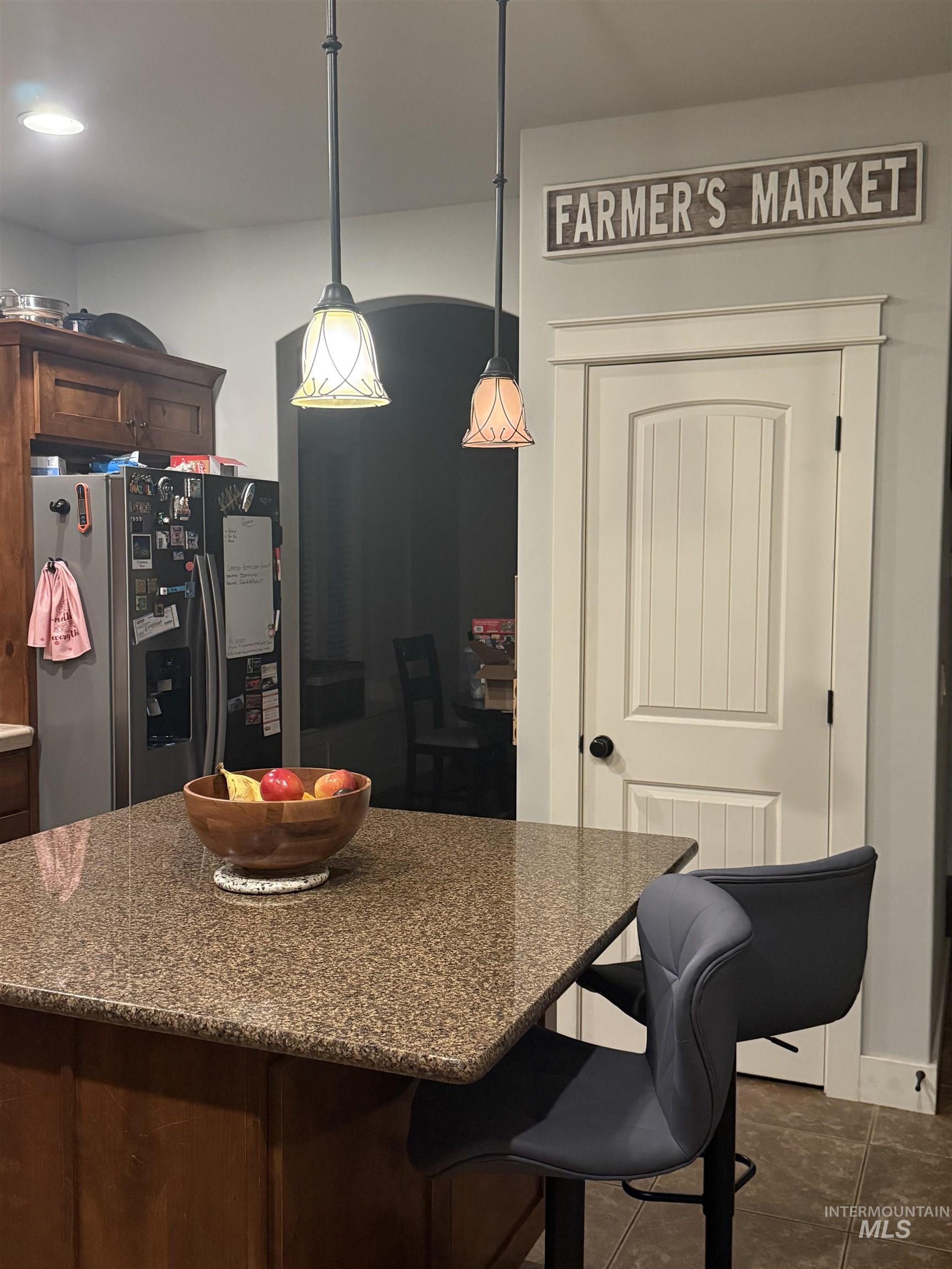 Kitchen featuring stainless steel fridge with ice dispenser, dark tile patterned flooring, hanging light fixtures, a breakfast bar area, and dark stone counters