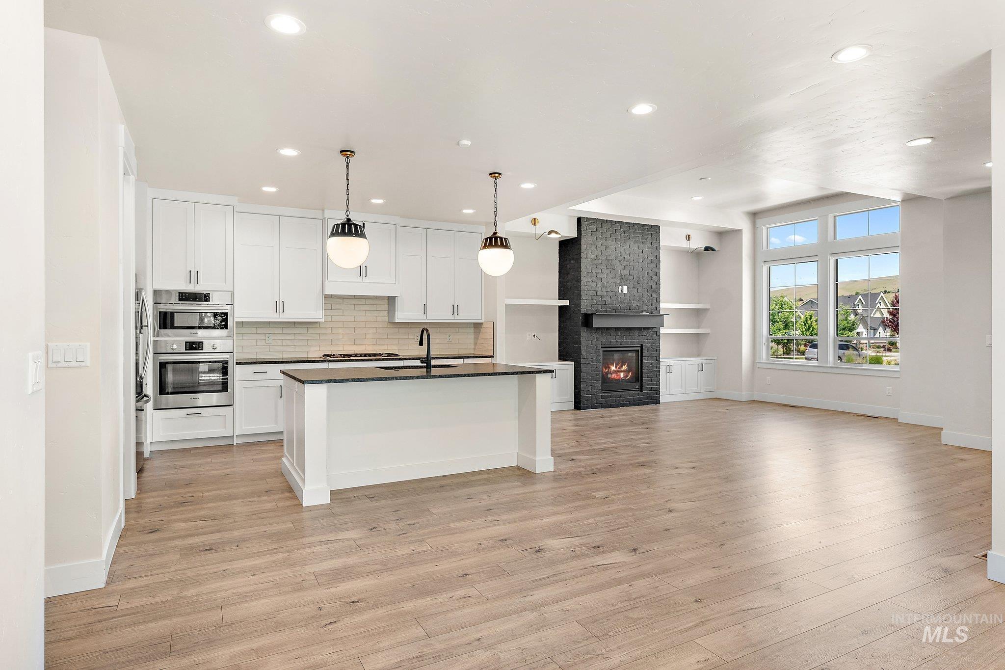Kitchen featuring white cabinets, pendant lighting, open floor plan, tasteful backsplash, and a large fireplace