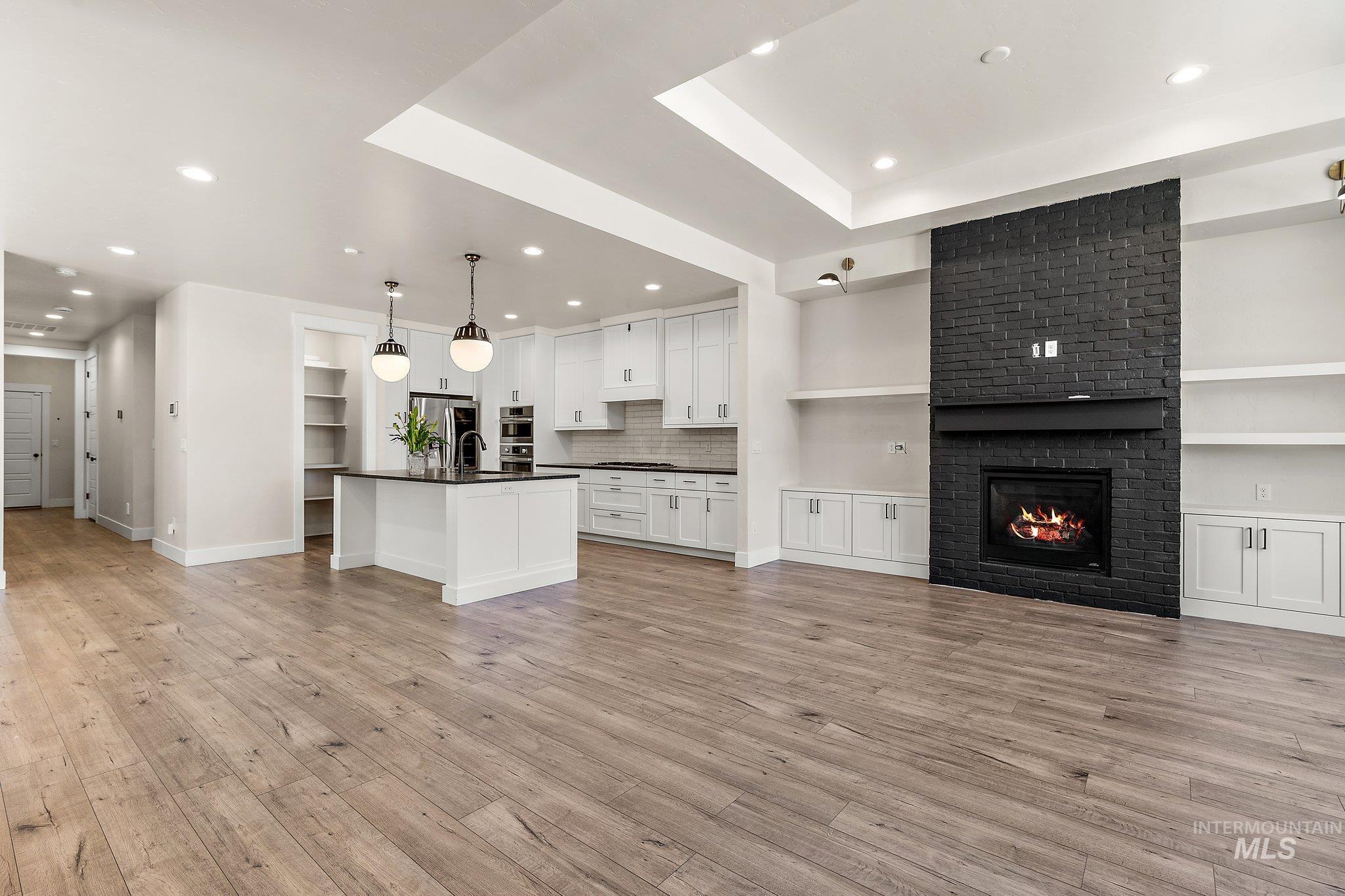 Kitchen featuring open floor plan, open shelves, white cabinetry, hanging light fixtures, and dark countertops