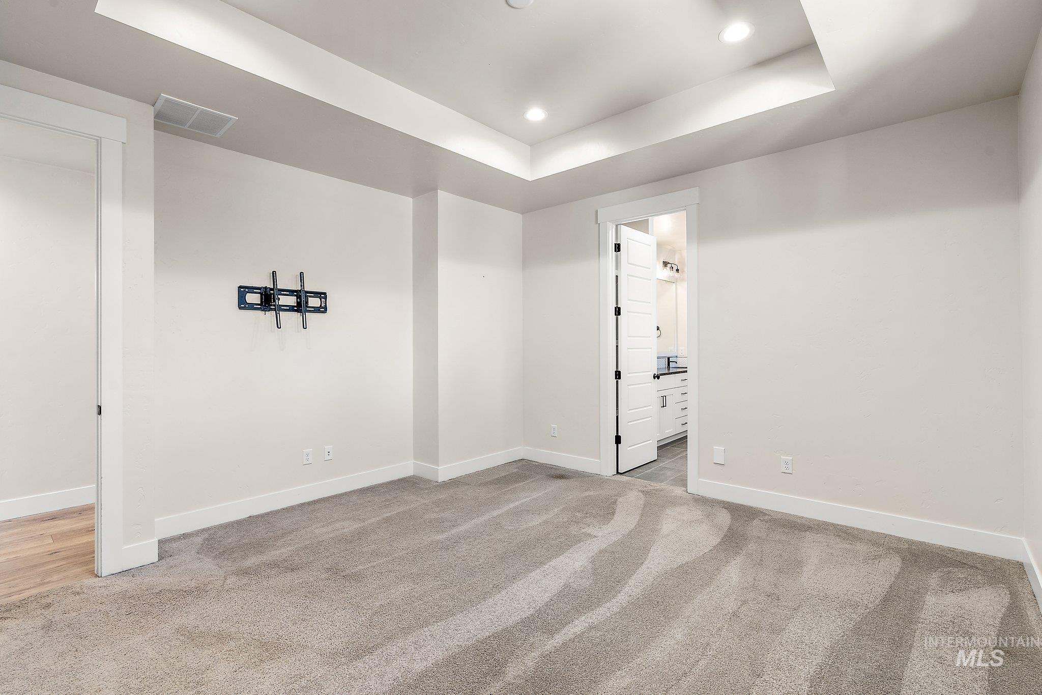 Empty room featuring a raised ceiling, light carpet, and recessed lighting