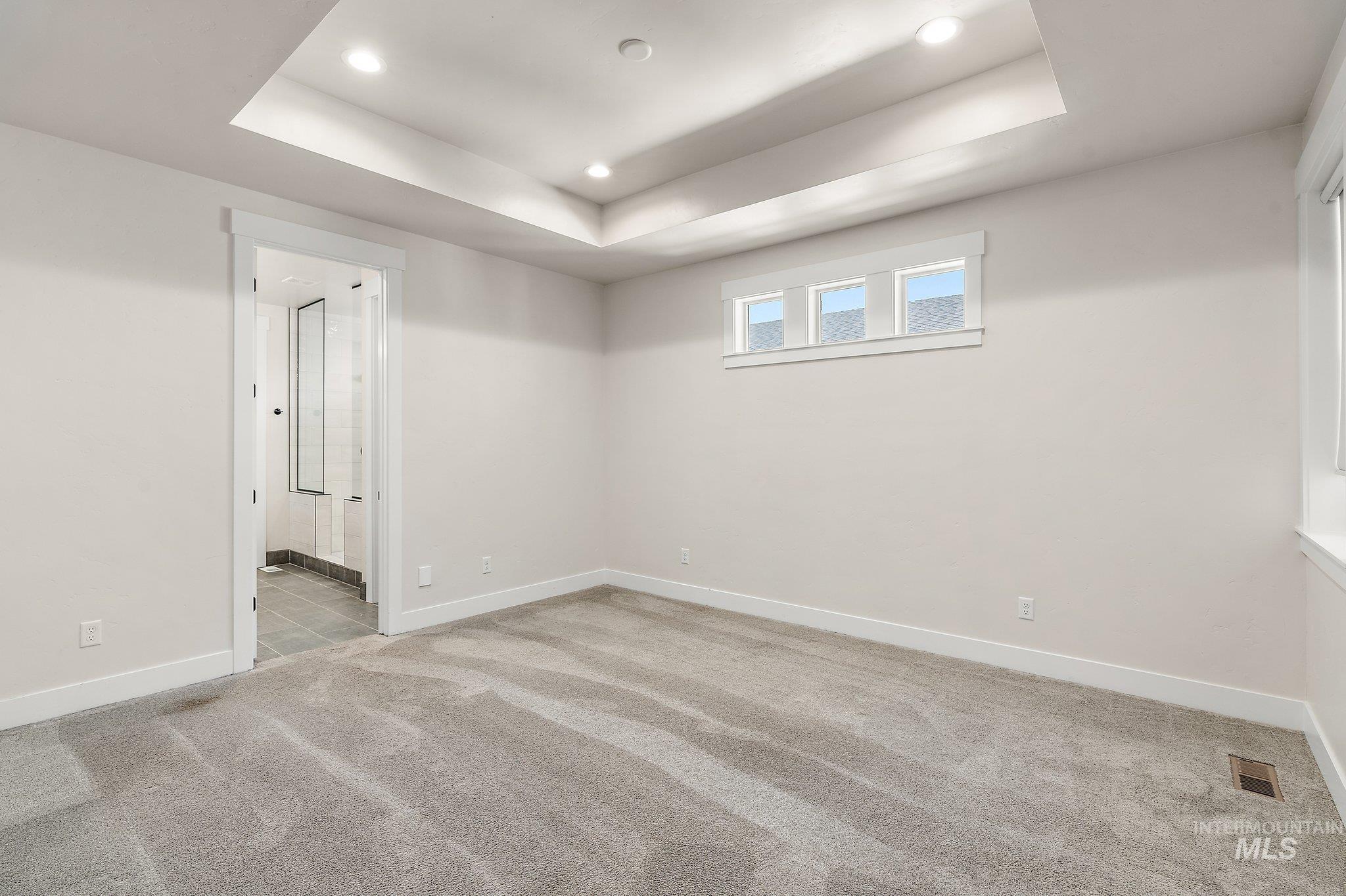 Empty room with a raised ceiling, light colored carpet, and recessed lighting