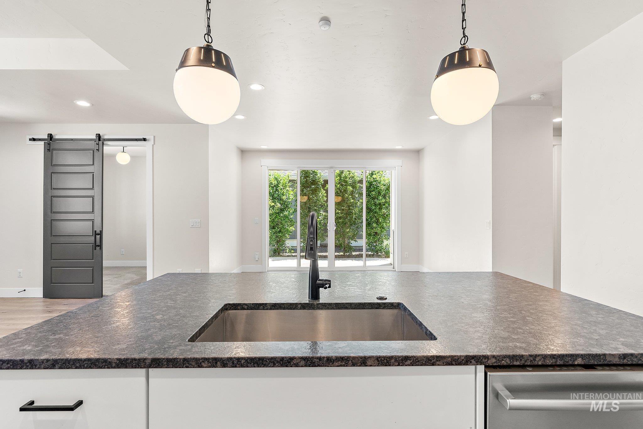 Kitchen featuring a barn door, pendant lighting, white cabinetry, dark stone counters, and recessed lighting