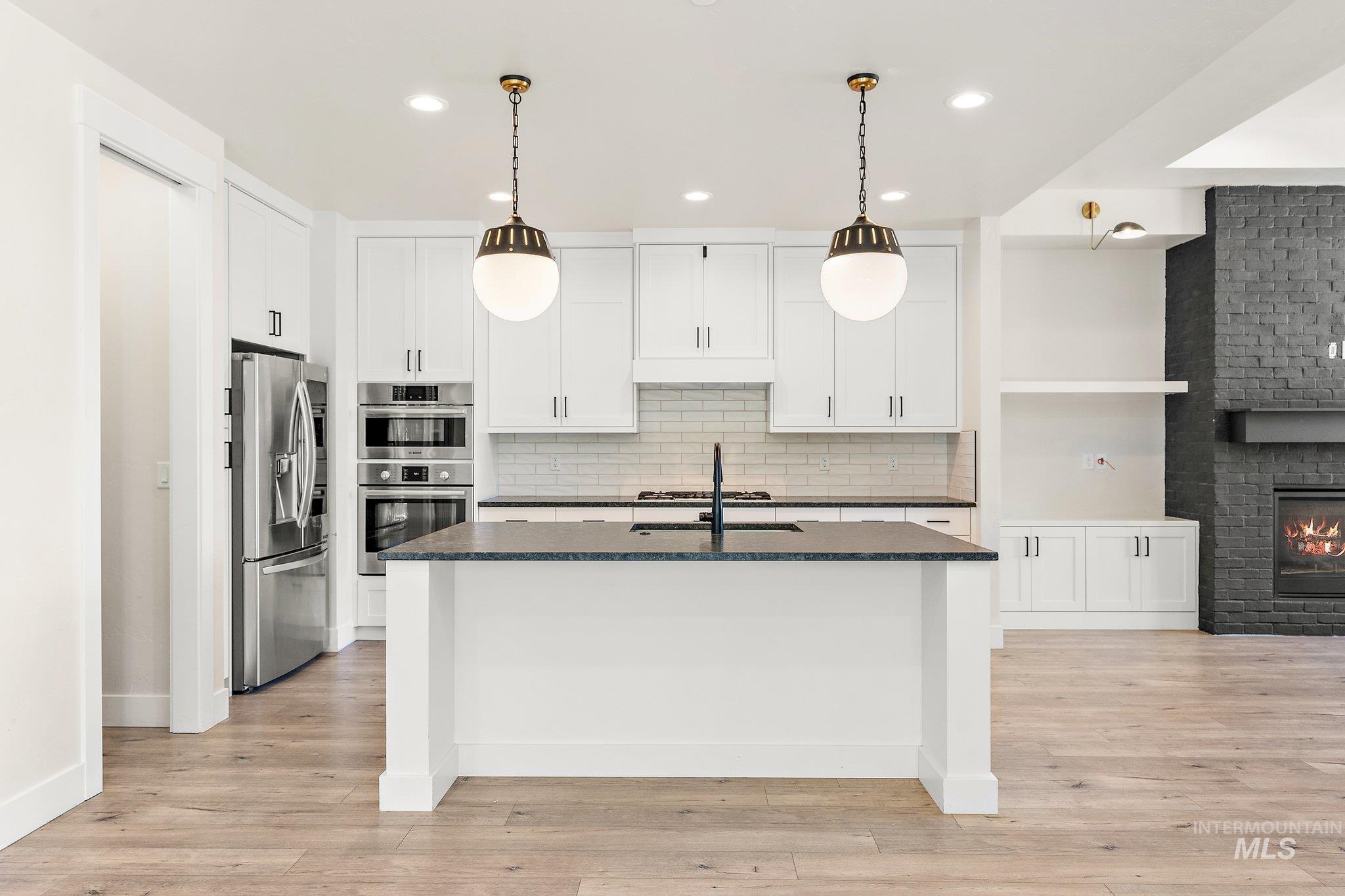 Kitchen with white cabinets, pendant lighting, decorative backsplash, stainless steel appliances, and dark stone countertops