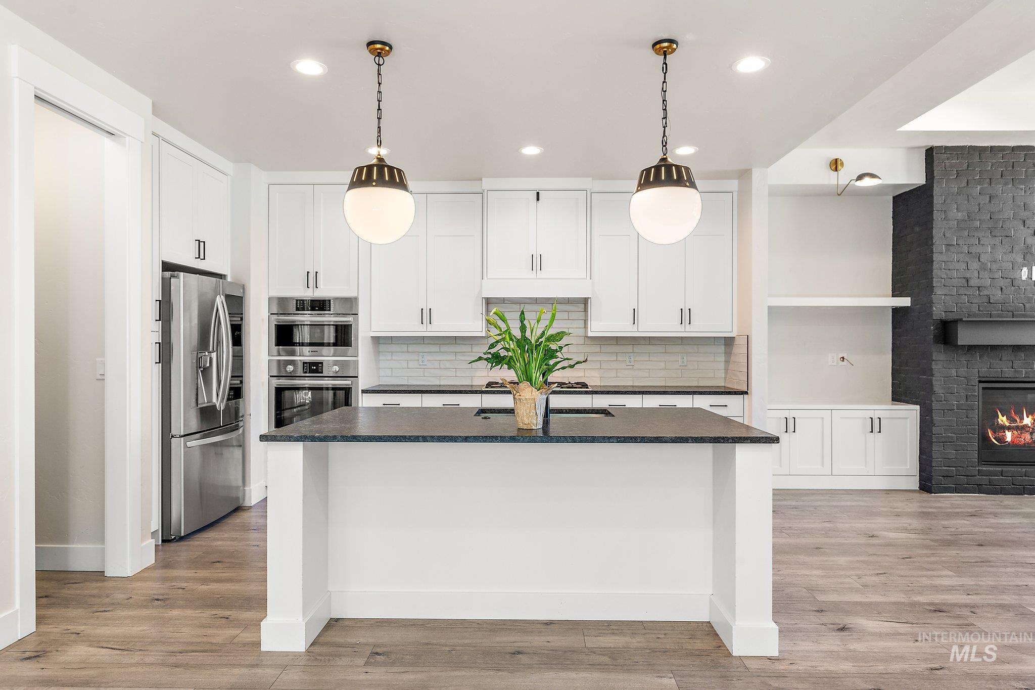 Kitchen with pendant lighting, white cabinets, appliances with stainless steel finishes, backsplash, and dark stone counters