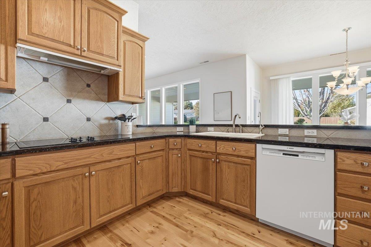 Kitchen with dishwasher, decorative backsplash, light wood-type flooring, brown cabinets, and healthy amount of natural light