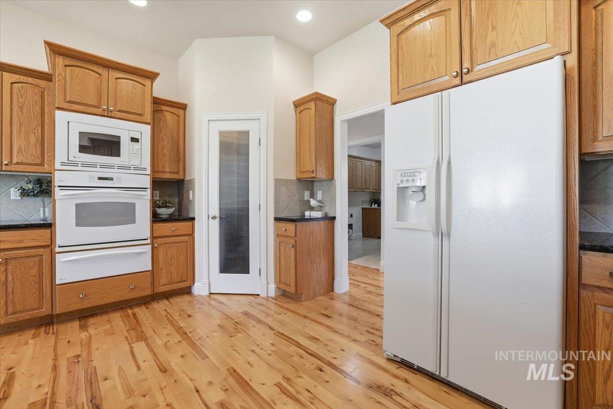 Kitchen with white appliances, backsplash, light wood-type flooring, a warming drawer, and brown cabinetry