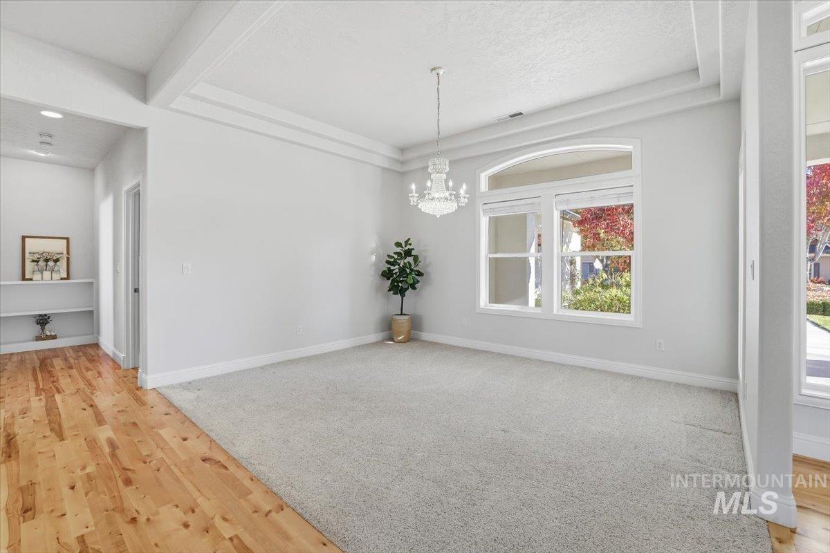 Unfurnished dining area with a chandelier, light wood-style floors, a textured ceiling, and beamed ceiling