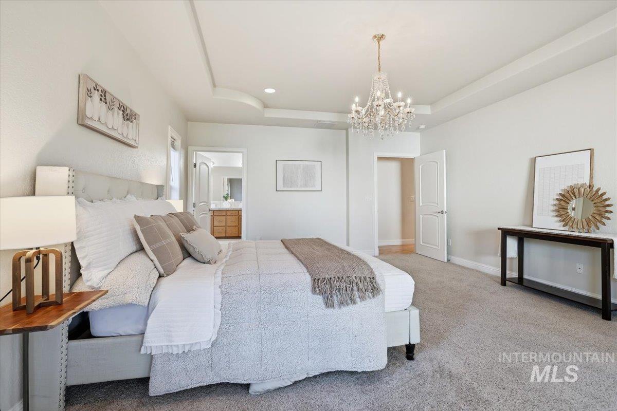 Bedroom with a tray ceiling, carpet flooring, ensuite bathroom, and a chandelier