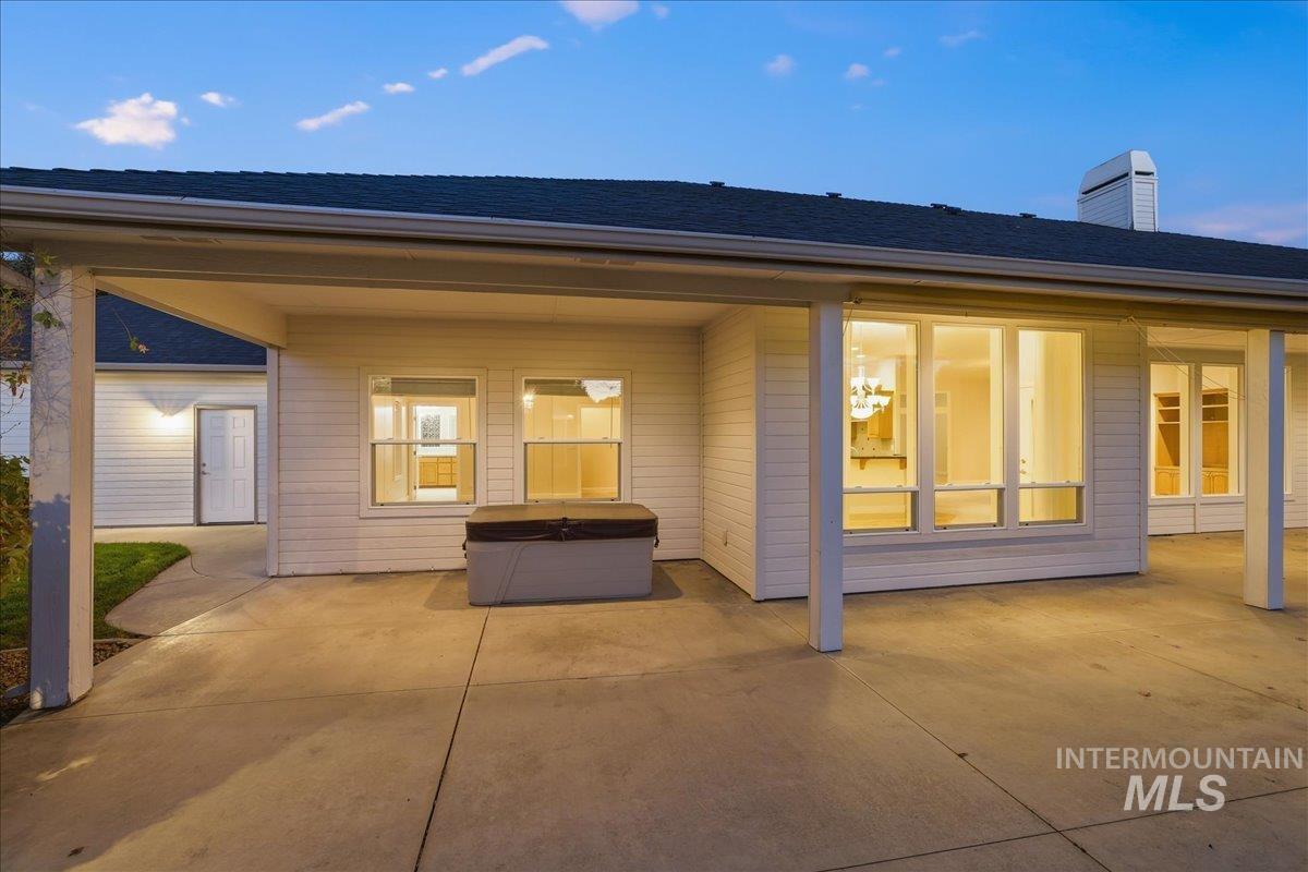 Back of property featuring a hot tub, a patio, a chimney, and a shingled roof