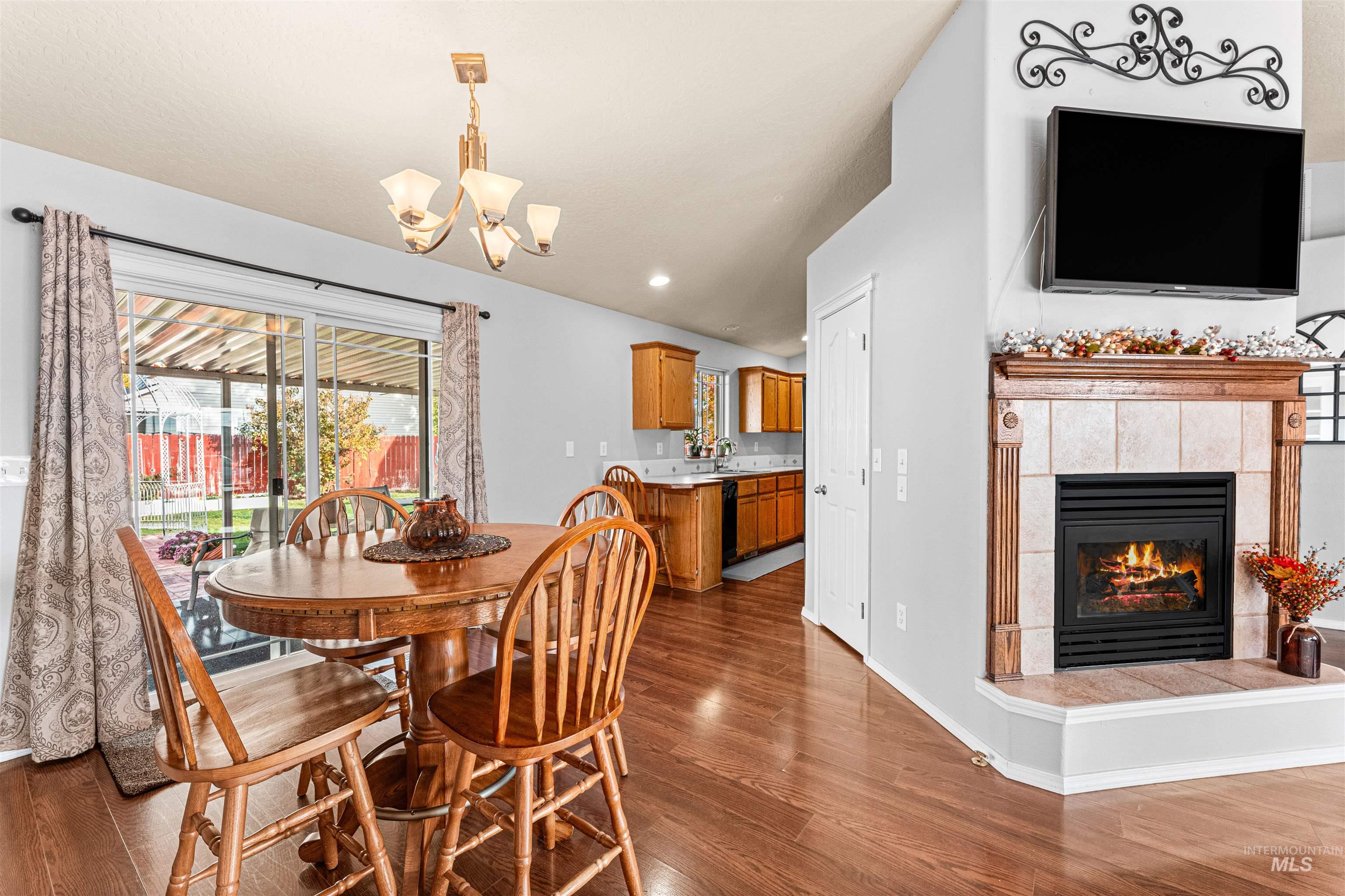 Dining area with a tiled fireplace, dark wood-type flooring, a chandelier, vaulted ceiling, and recessed lighting