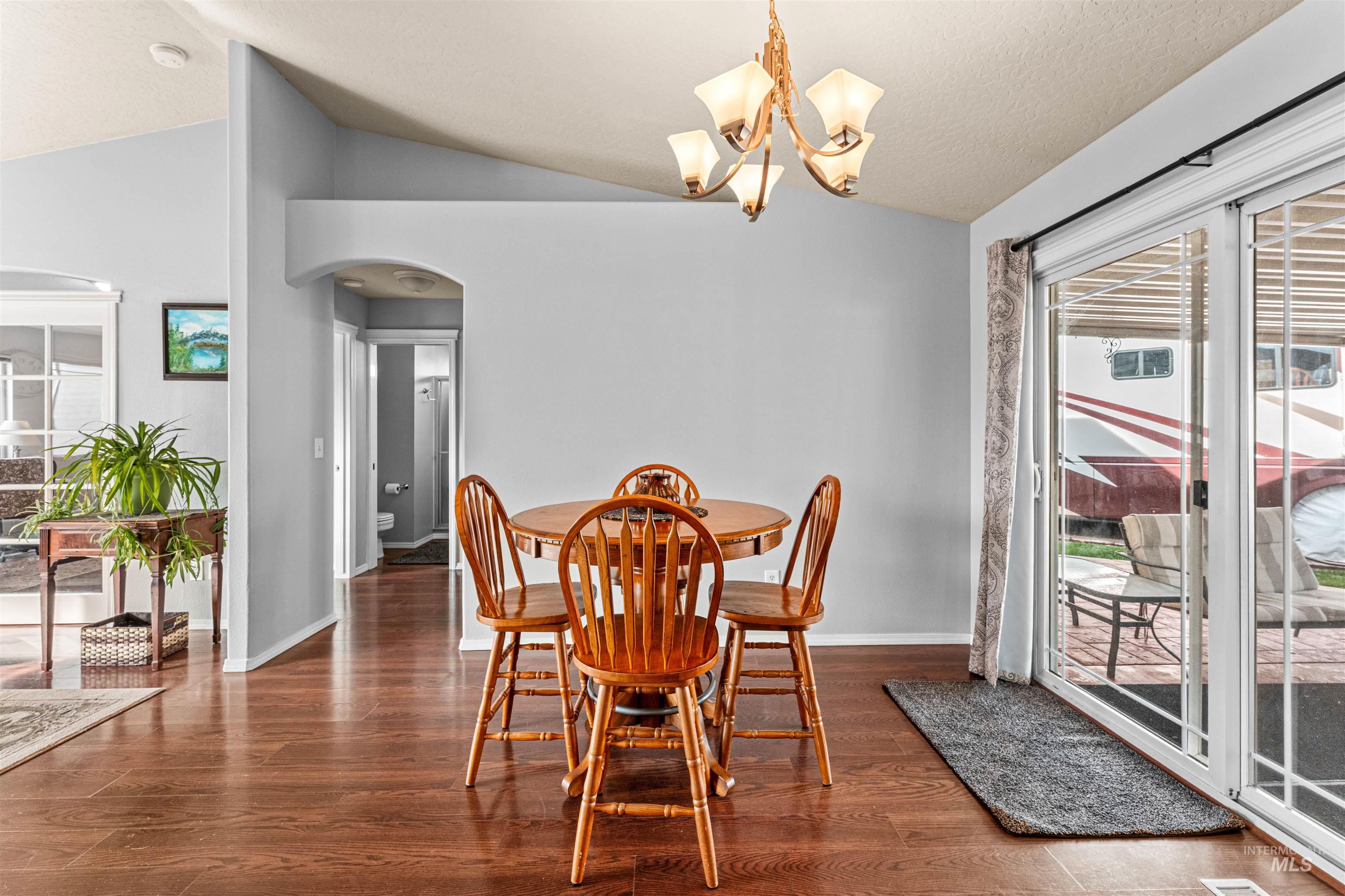 Dining area with dark wood-style floors, arched walkways, vaulted ceiling, and a chandelier