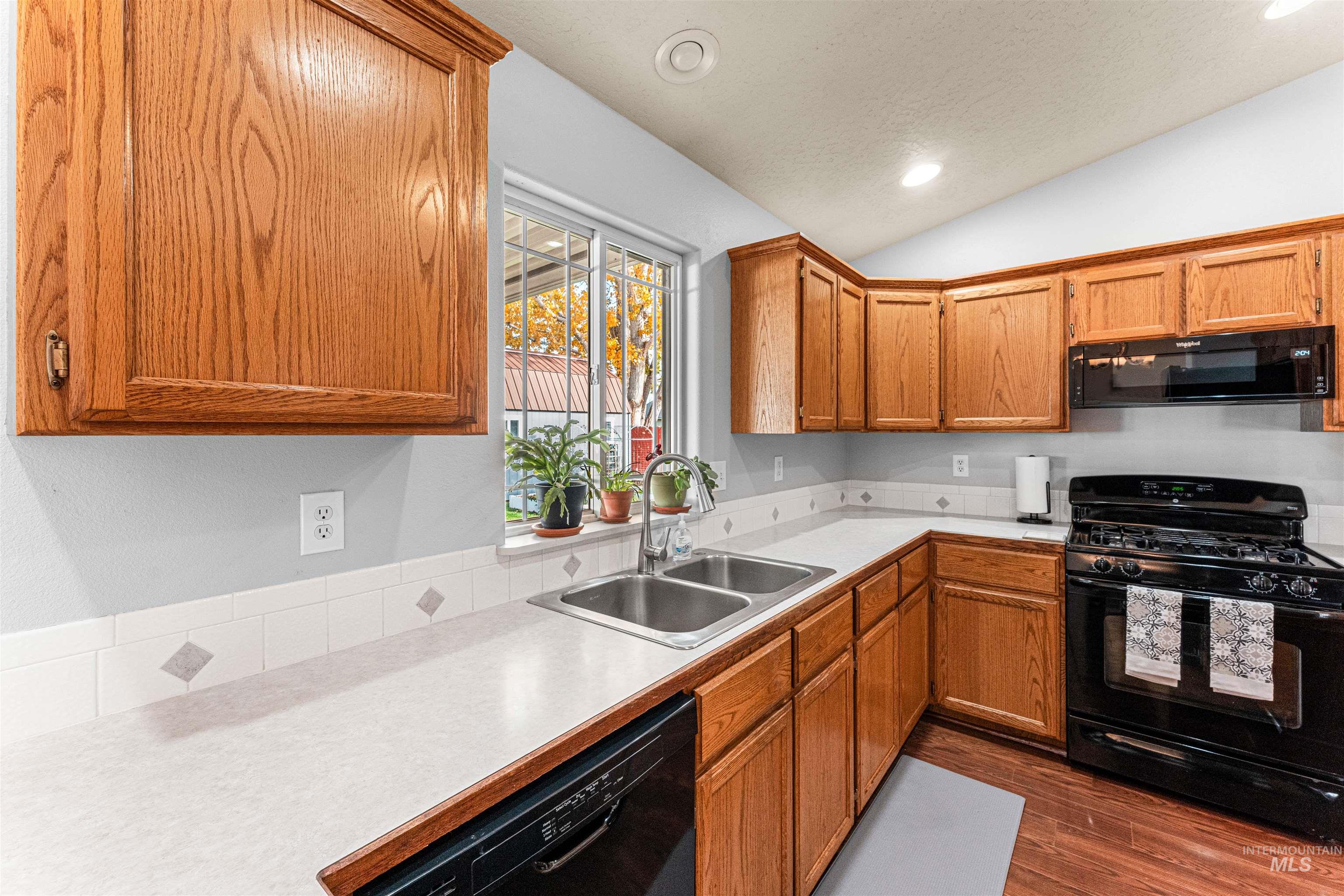 Kitchen with black appliances, light countertops, brown cabinets, recessed lighting, and dark wood-style floors