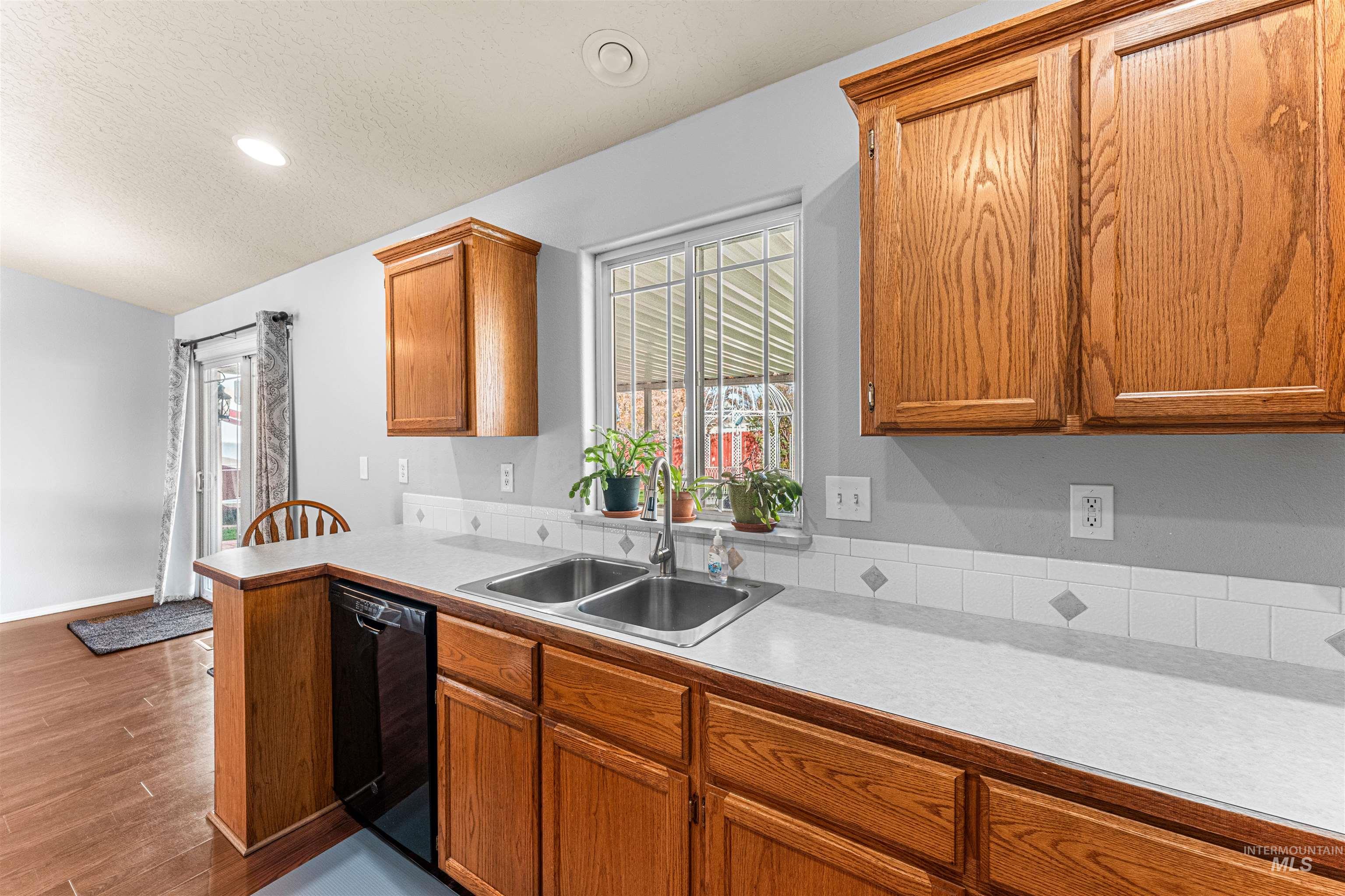 Kitchen with light countertops, a textured ceiling, brown cabinets, dishwasher, and dark wood-style flooring