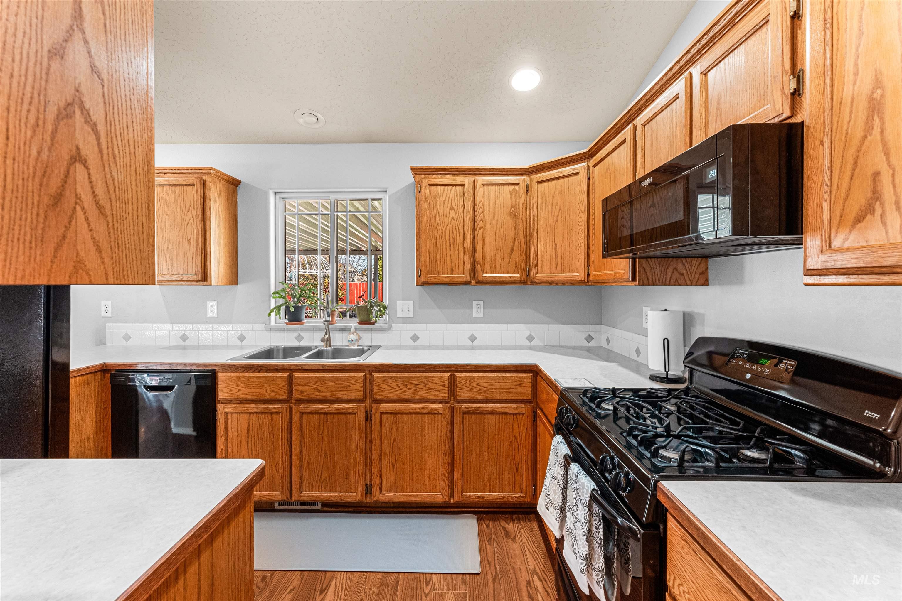 Kitchen featuring black appliances, brown cabinetry, dark wood finished floors, and recessed lighting