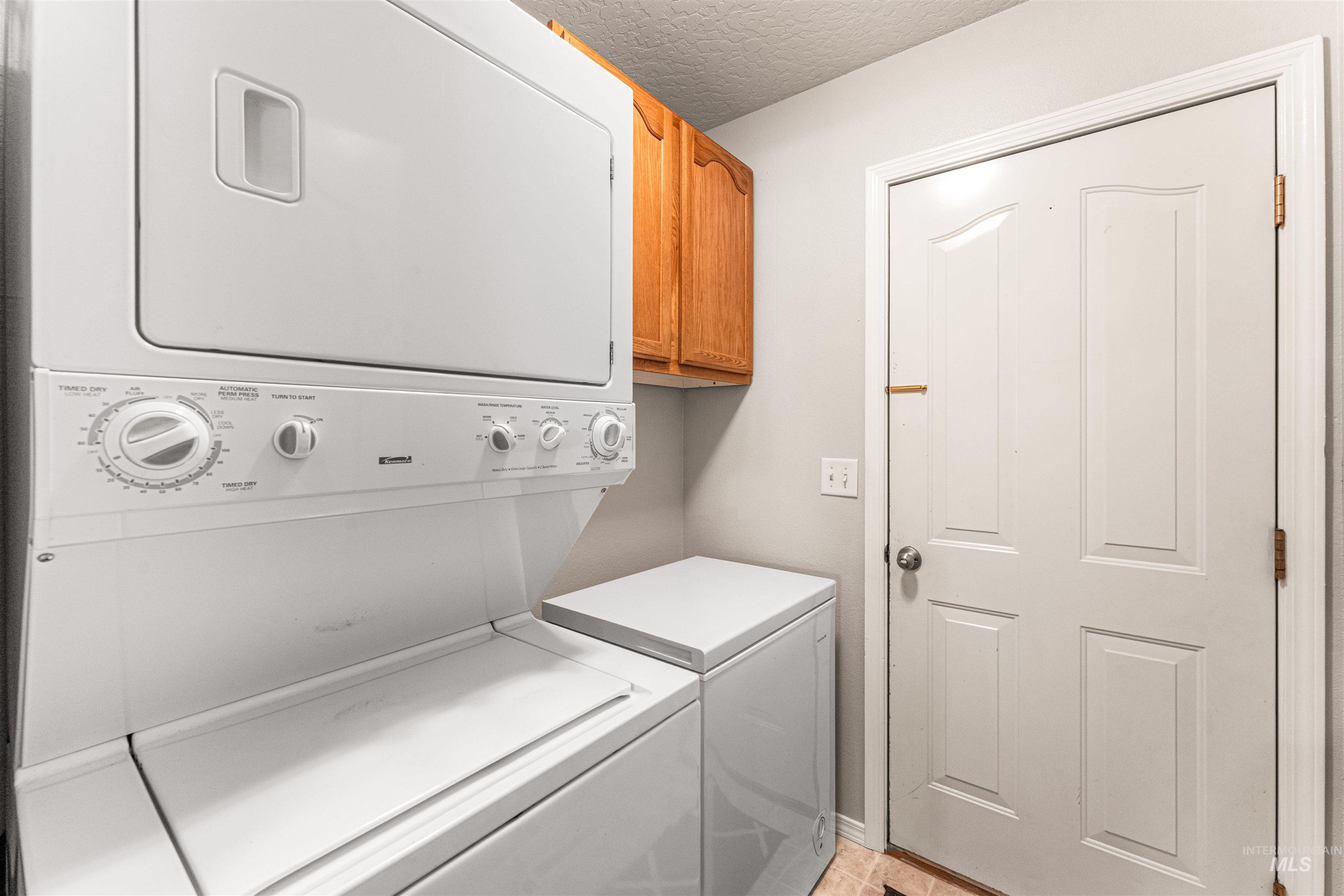 Washroom featuring stacked washer and clothes dryer, a textured ceiling, and cabinet space