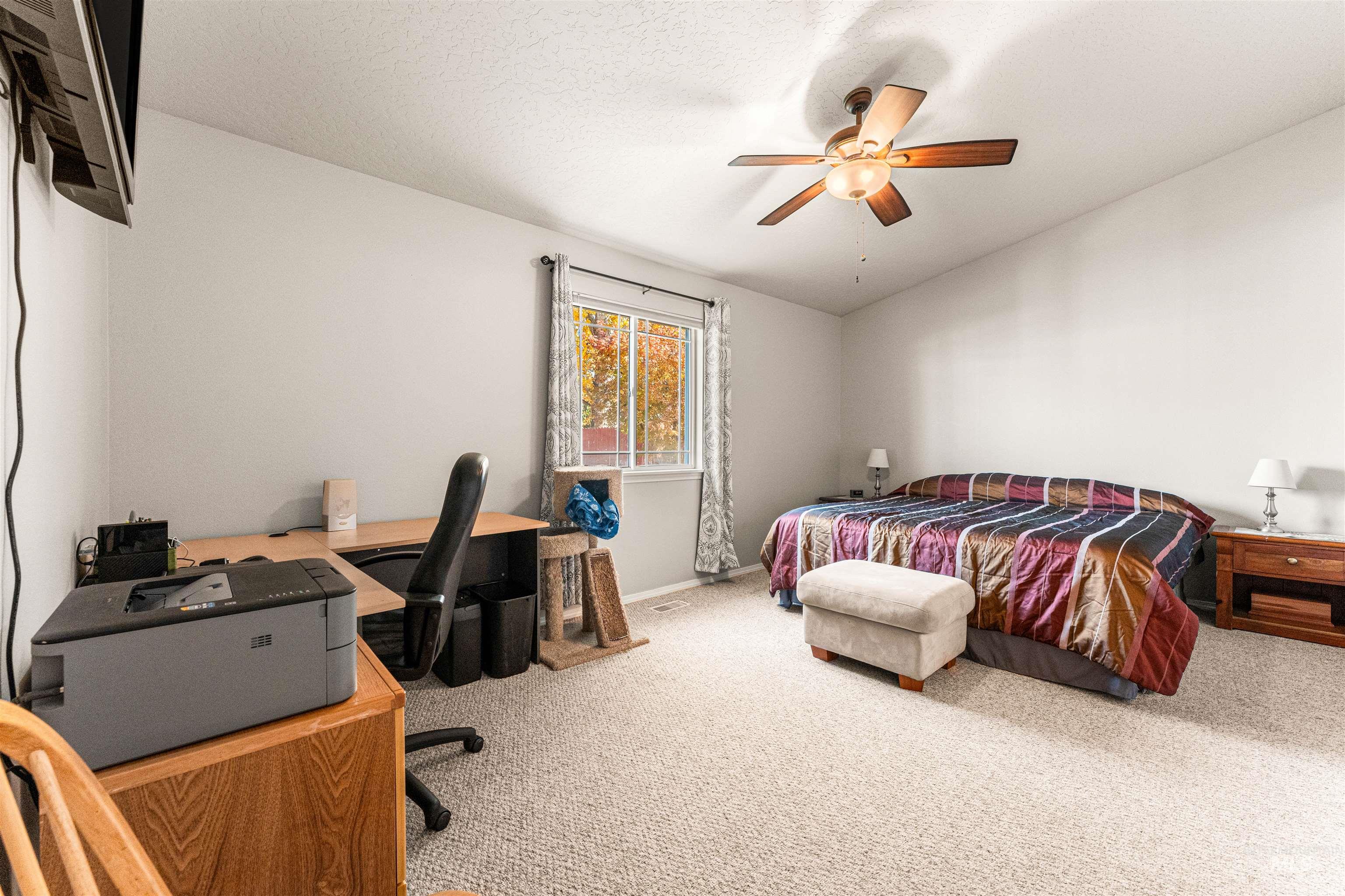 Bedroom featuring light carpet, vaulted ceiling, ceiling fan, an office area, and a textured ceiling