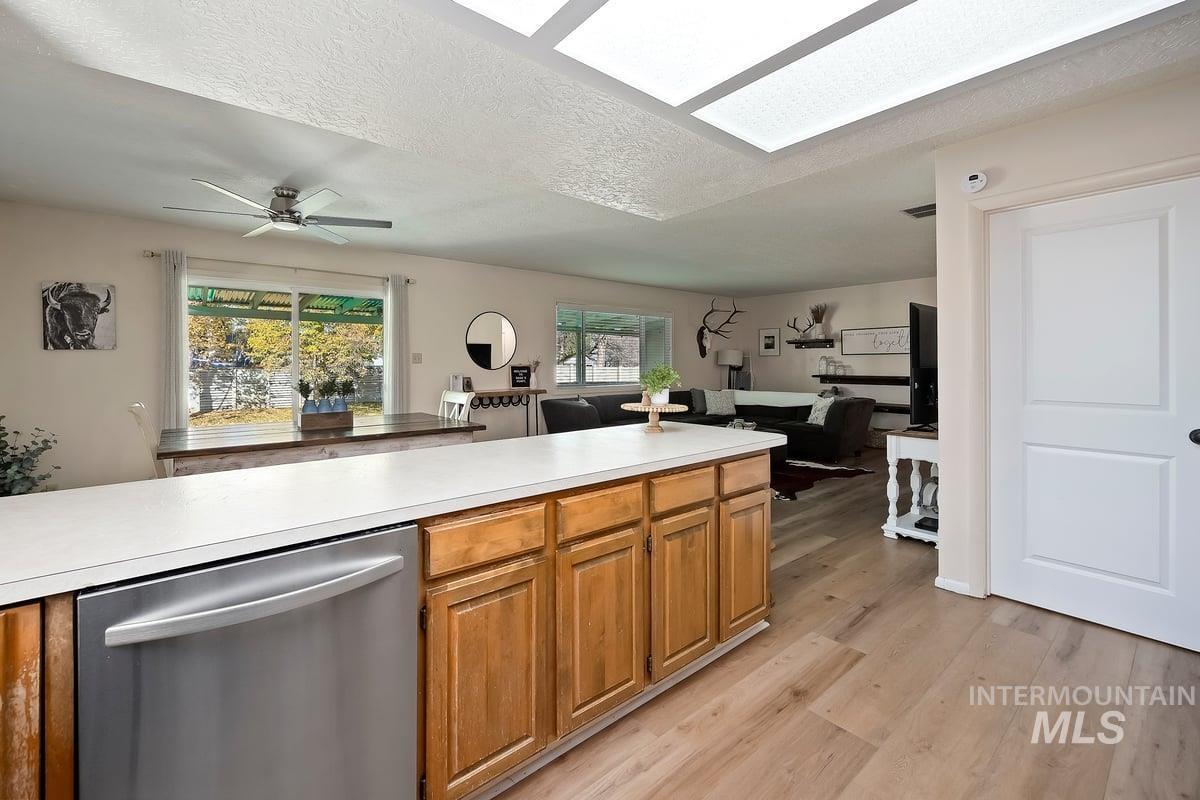 Kitchen with light countertops, stainless steel dishwasher, a textured ceiling, brown cabinetry, and open floor plan
