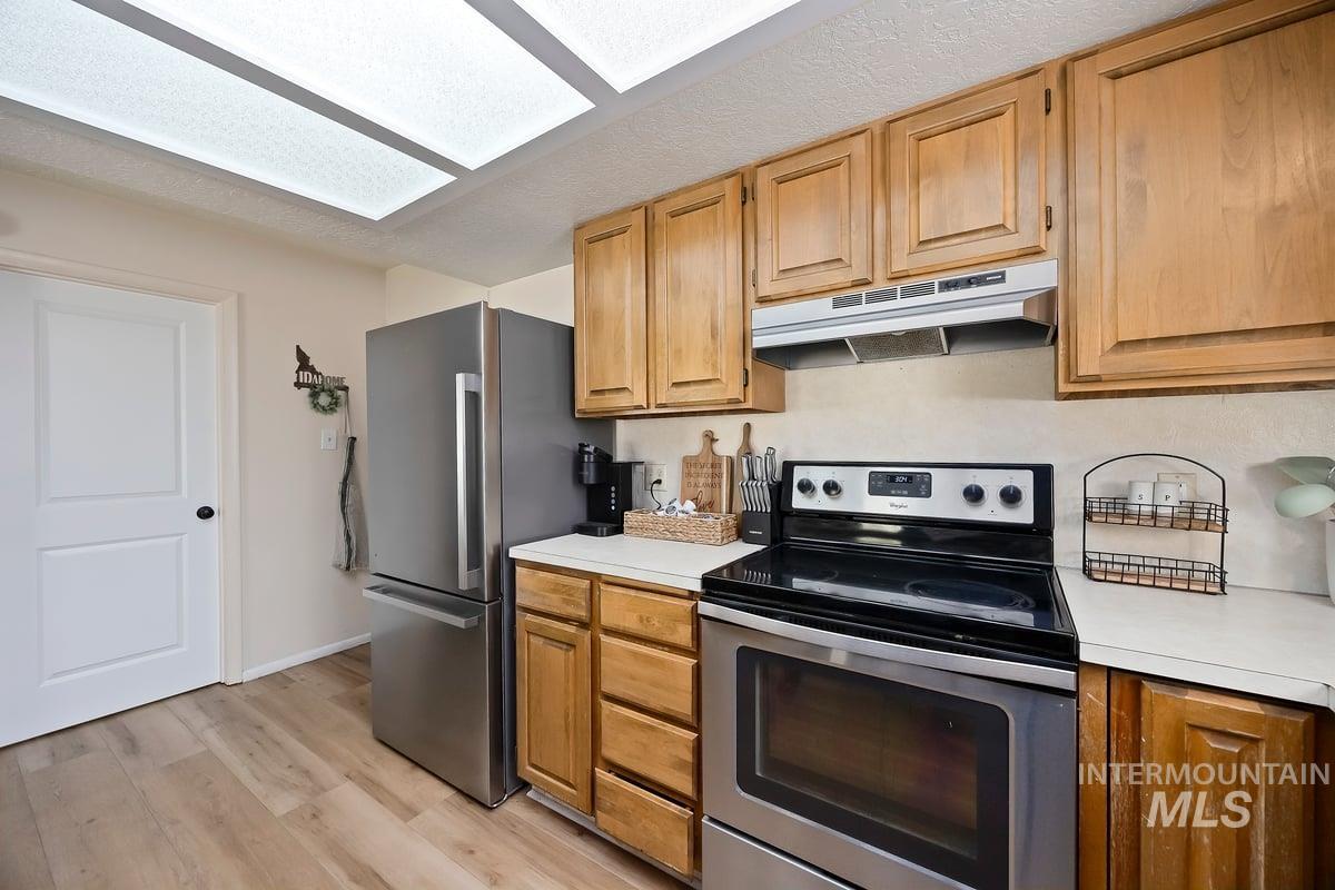 Kitchen with appliances with stainless steel finishes, light countertops, under cabinet range hood, light wood-style flooring, and a textured ceiling
