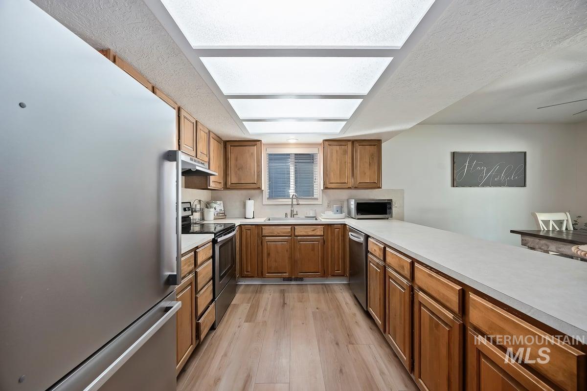 Kitchen featuring appliances with stainless steel finishes, brown cabinetry, light countertops, light wood-style flooring, and a textured ceiling