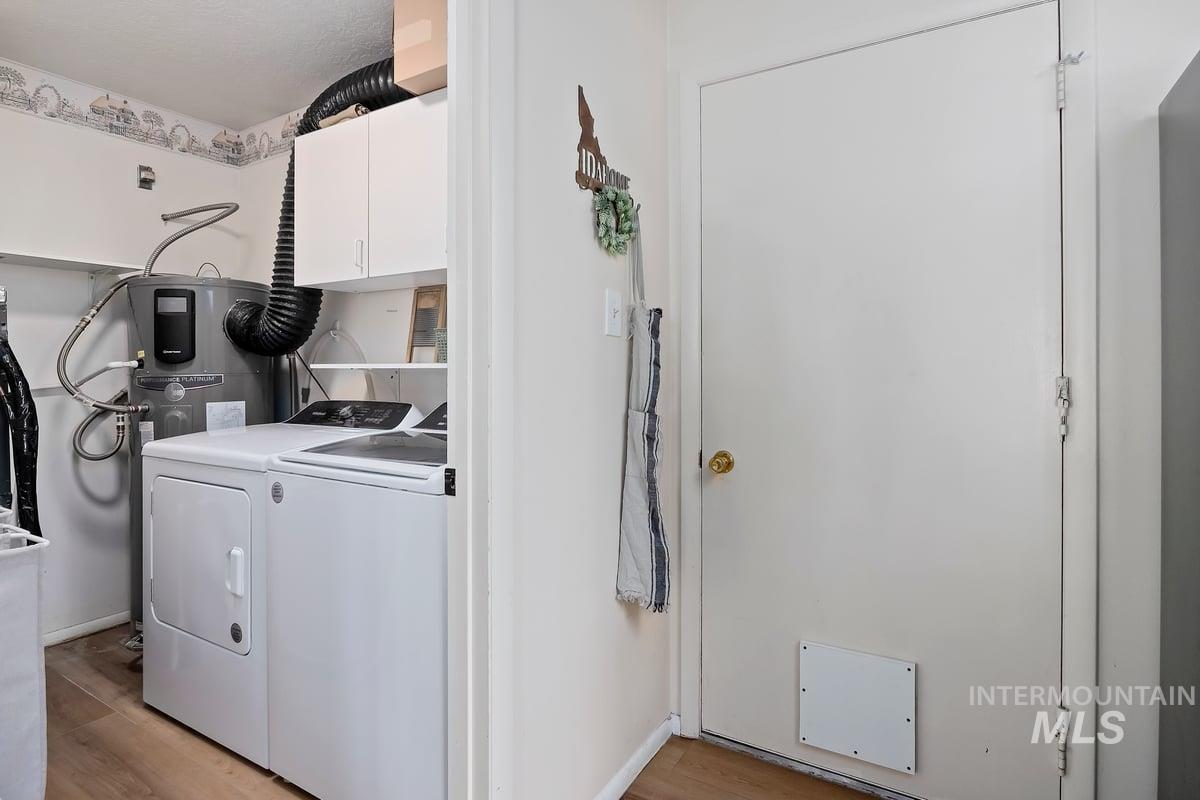 Washroom with cabinet space, light wood-style flooring, separate washer and dryer, and water heater